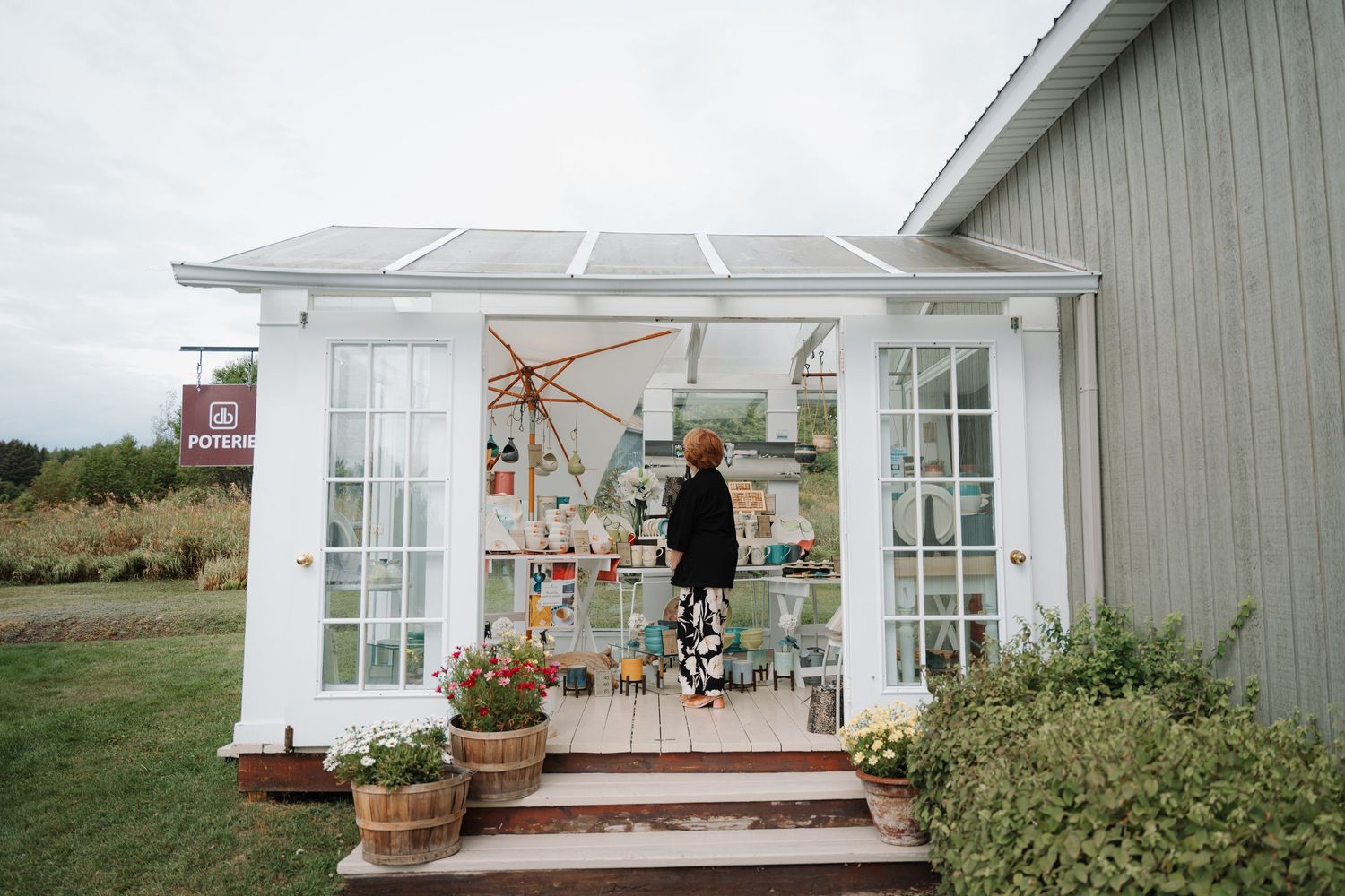 Woman standing in a charming glass greenhouse studio surrounded by artwork on a farm.