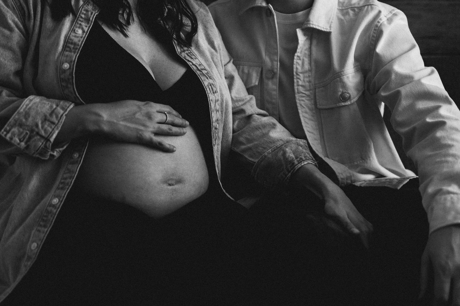 Black and white close-up of couple tenderly touching pregnant belly with ringed hands.