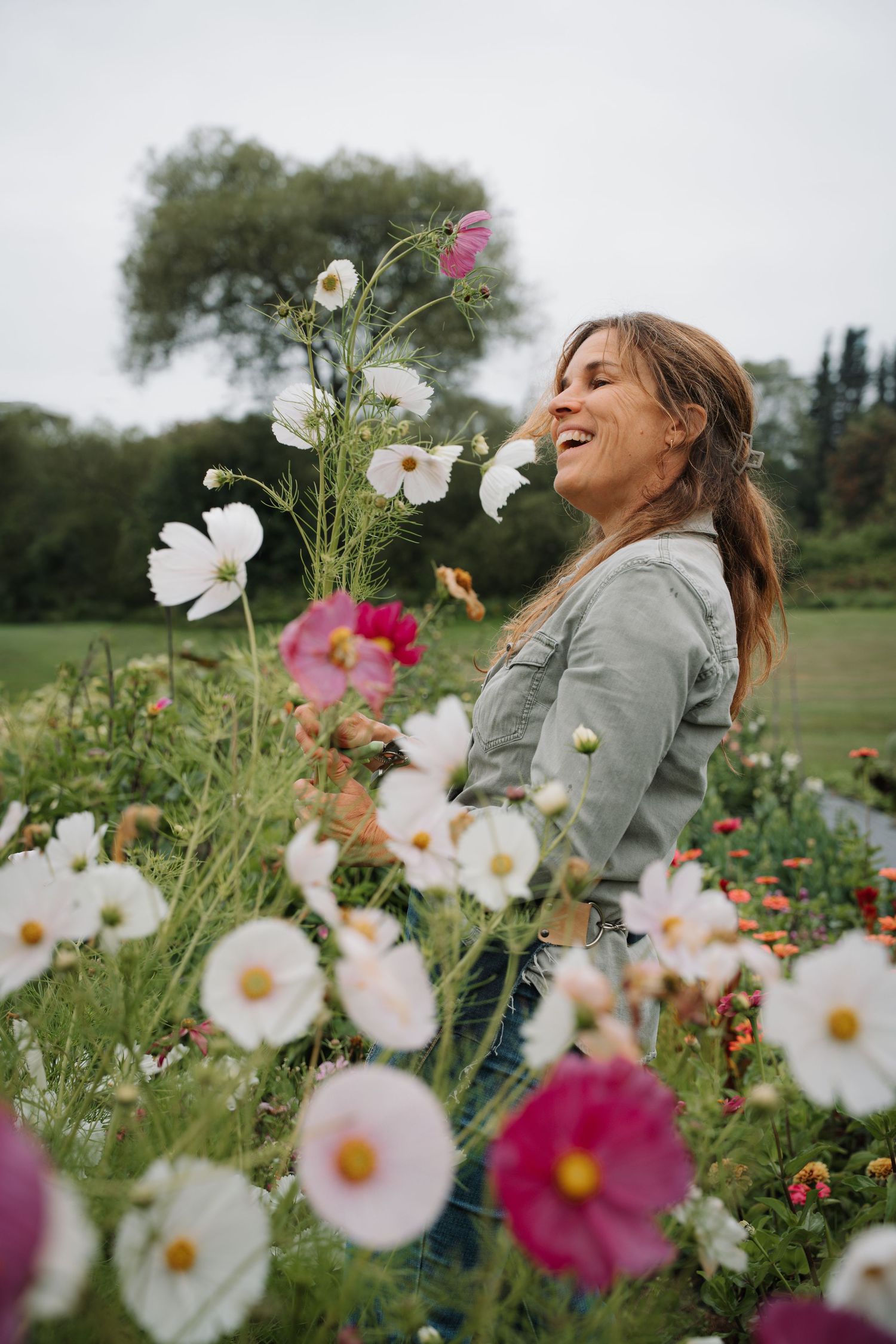 Smiling woman standing among blooming white and pink cosmos flowers in a garden.