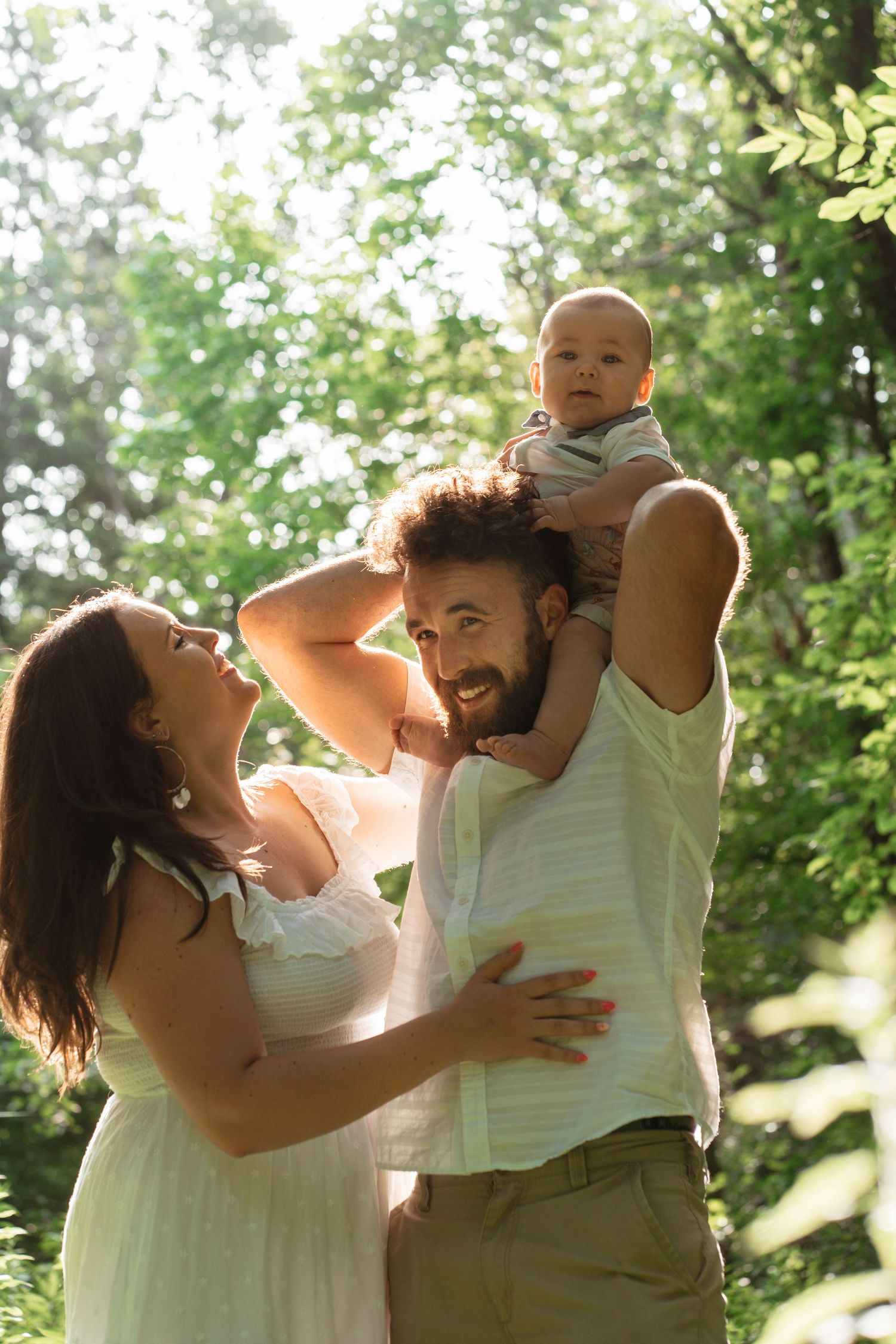 Happy family with a bearded father holding a baby outdoors in sunlight.