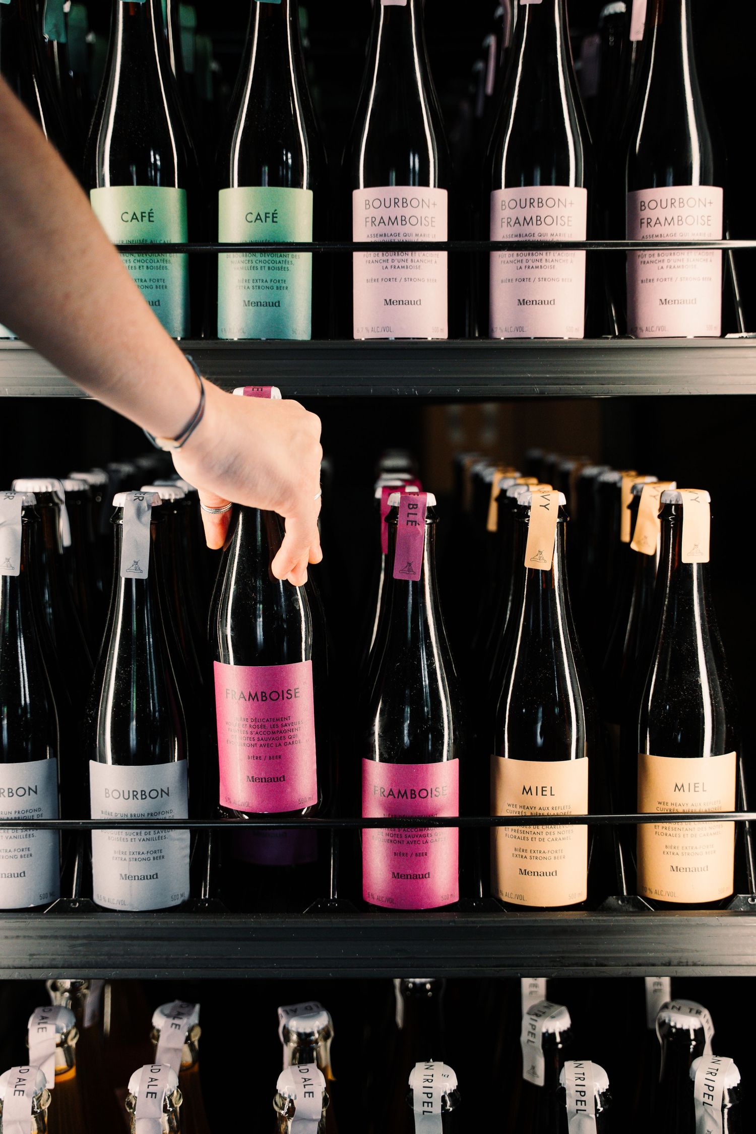 Hand selecting a pink-labeled bottle from a shelf of neatly arranged wine bottles in a wine shop.