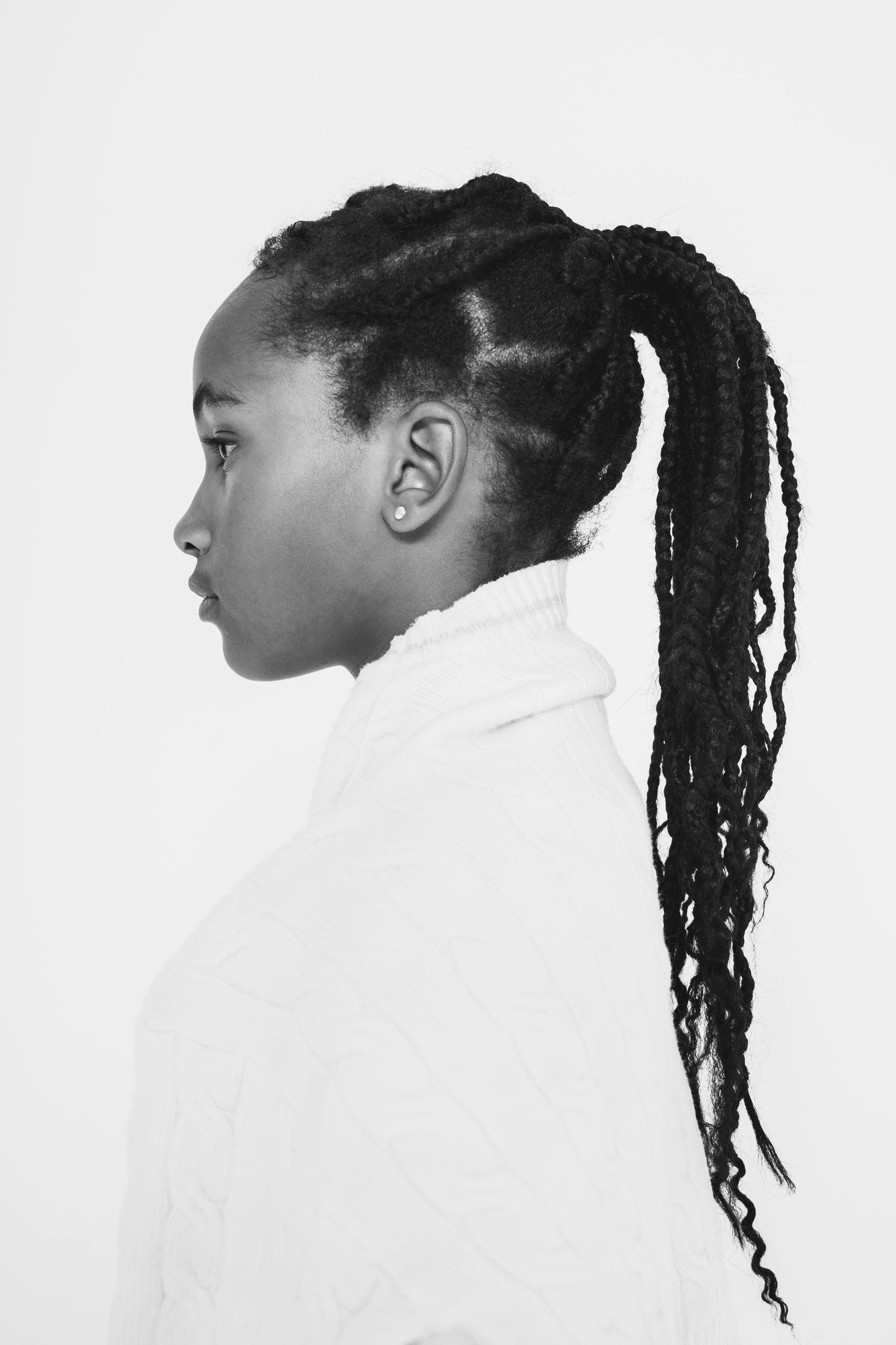 Black and white profile portrait of young woman with long braided ponytail in white top.