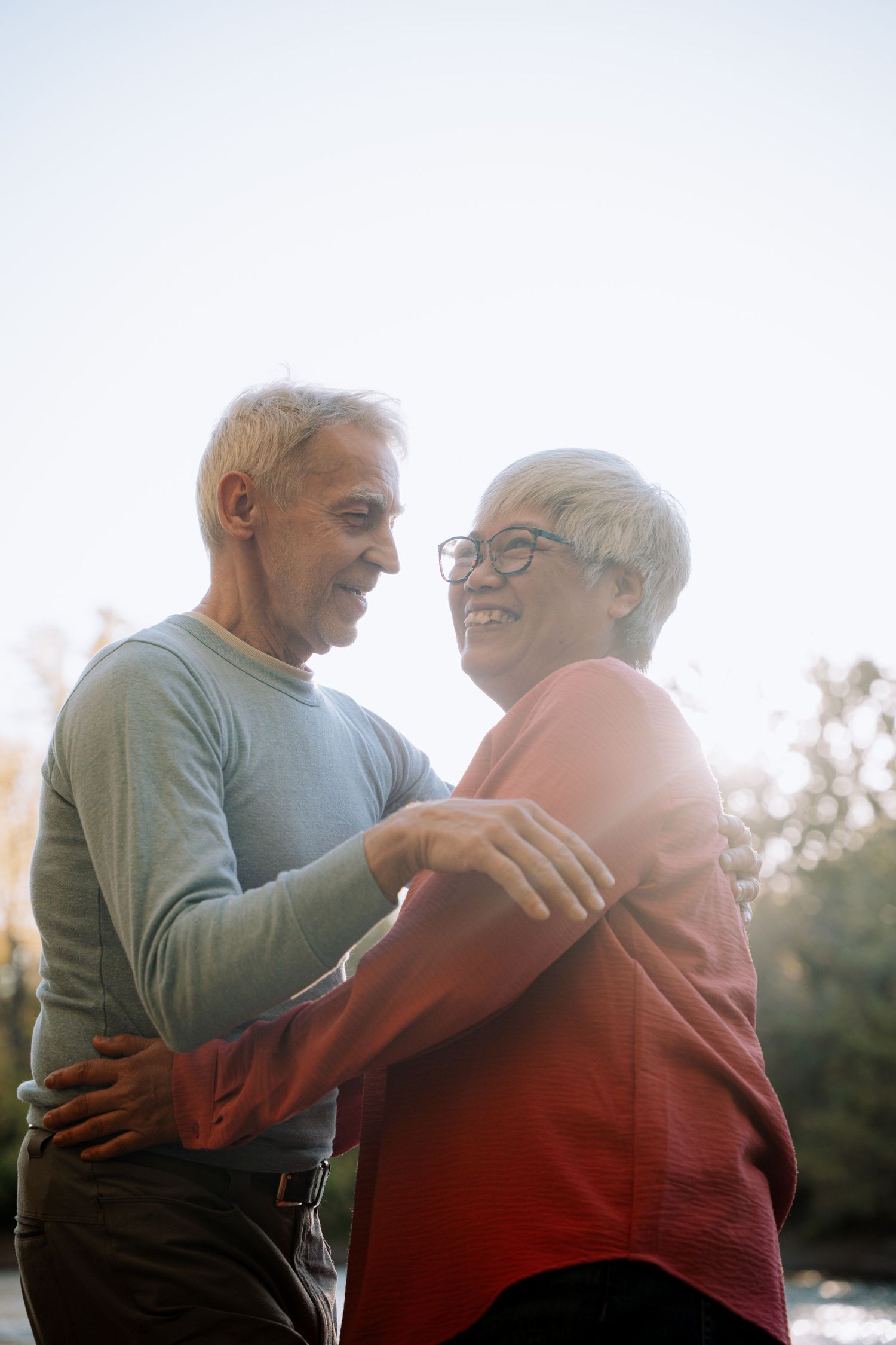 Joyful senior couple dancing outdoors in warm backlit sunlight.