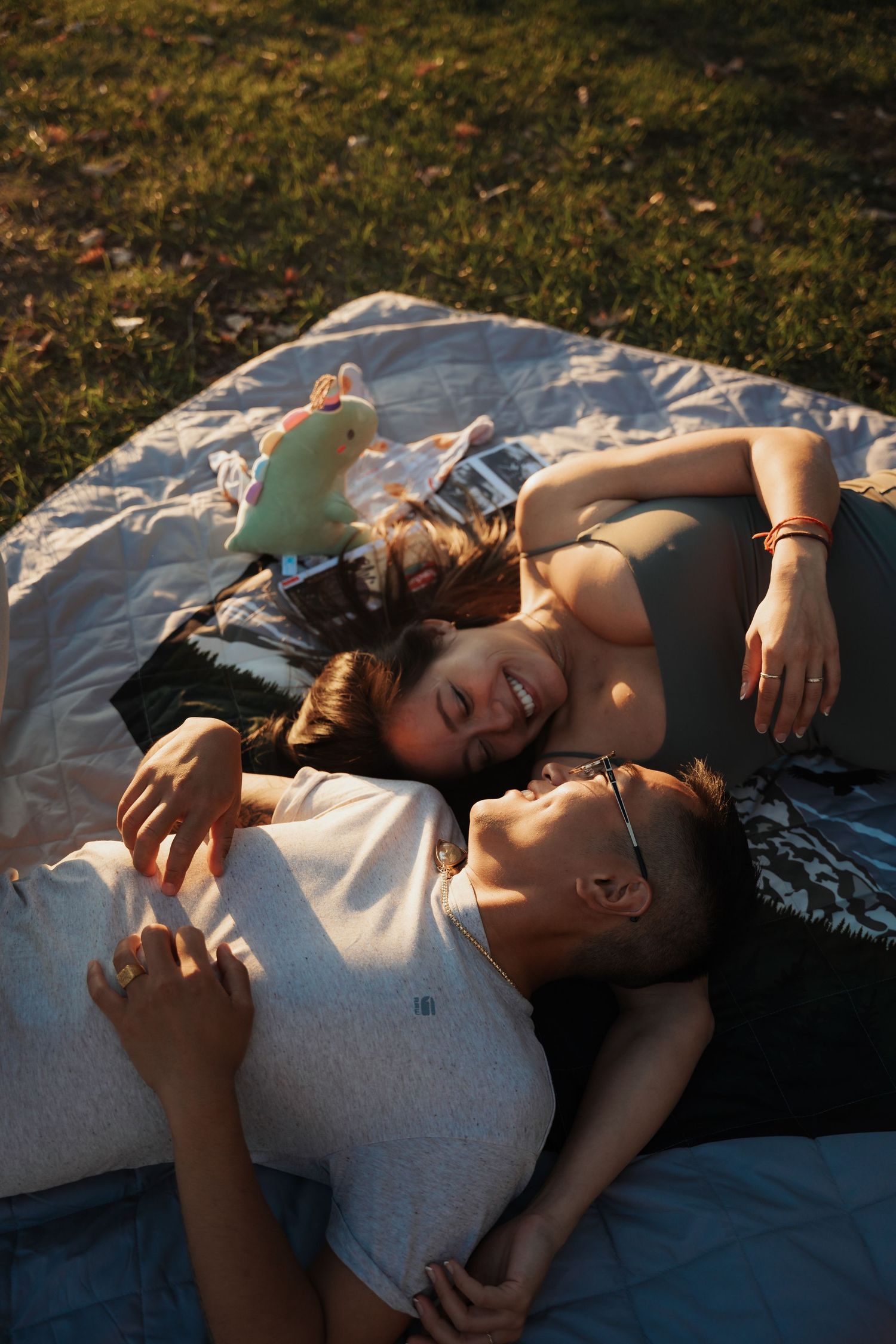 Smiling couple lying on a blanket in the grass together on a sunny day enjoying a relaxing outdoor moment.