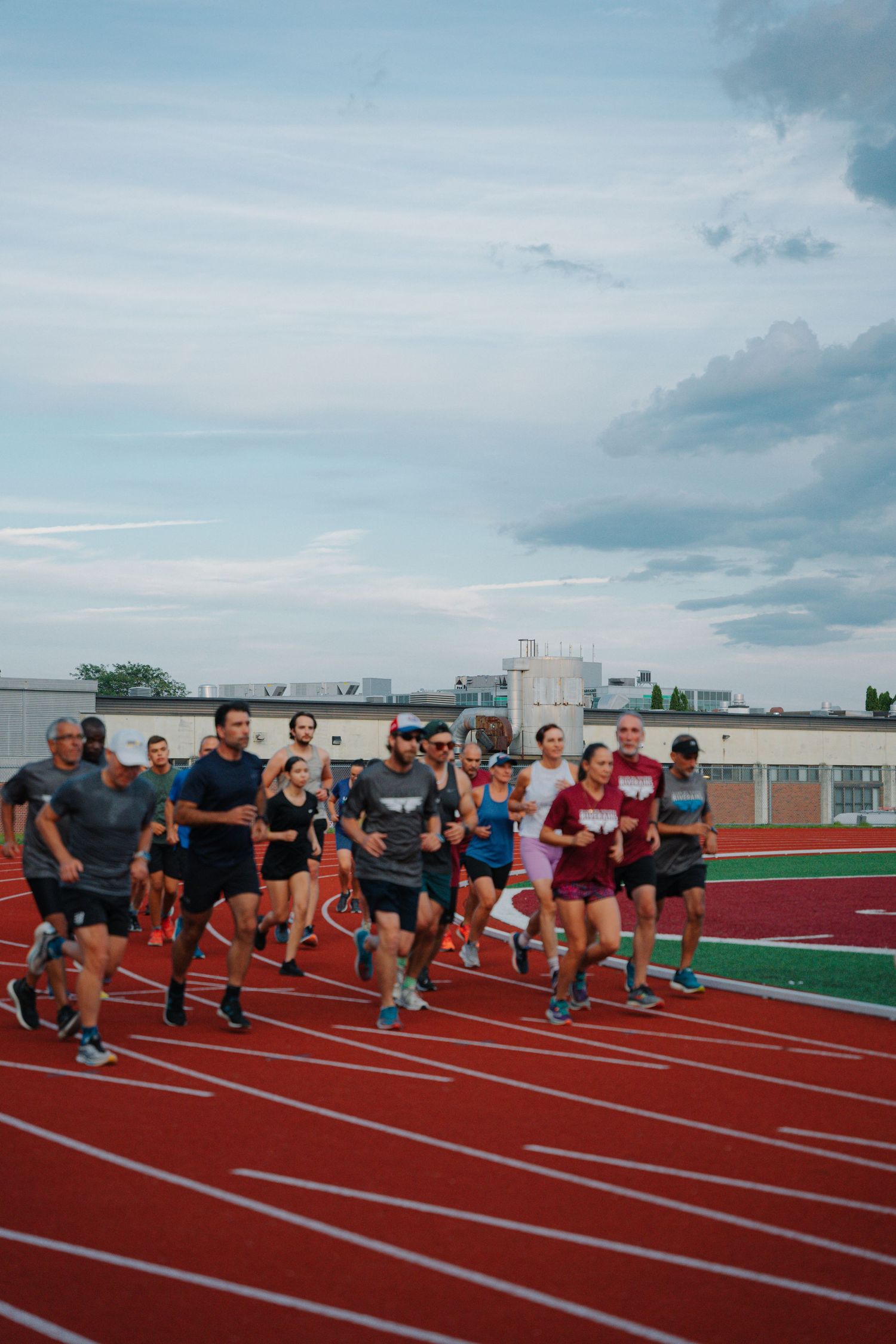 Group of runners training together on a red outdoor track under a cloudy sky.