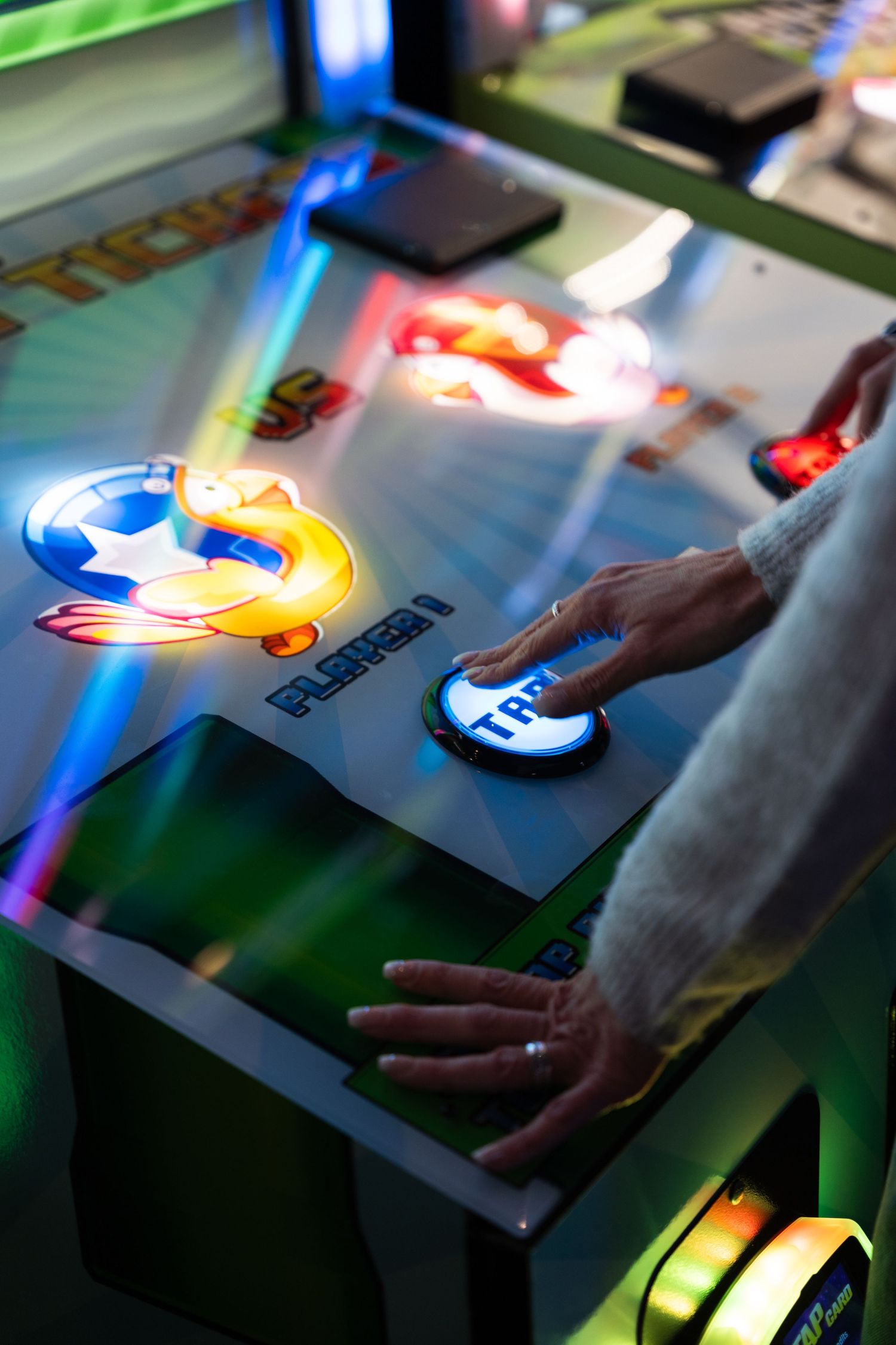 Close-up of hands pressing a glowing button on a colorful arcade game machine.