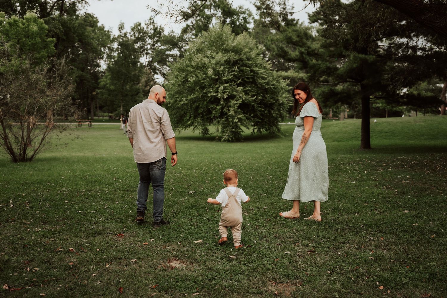 A young family with a toddler enjoying a walk in a lush green park during a warm summer day.