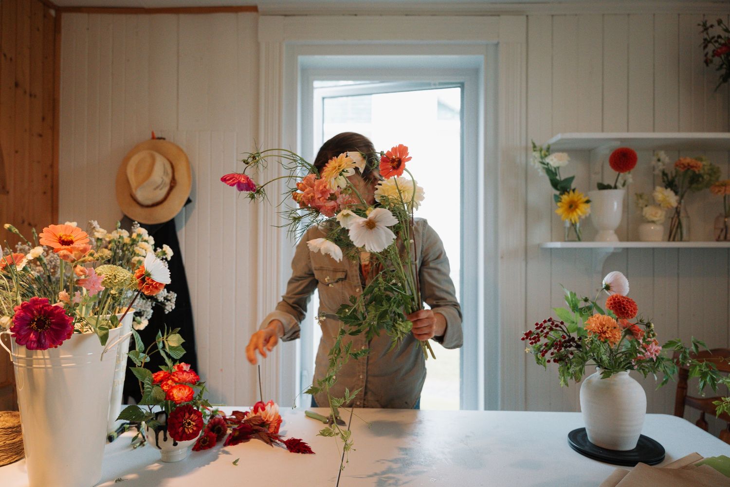 Florist holding a large bouquet of mixed flowers in a white-walled flower studio.