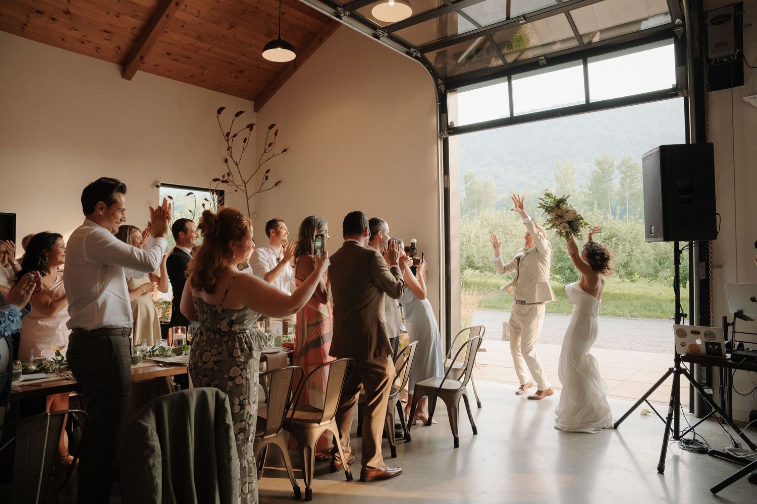 Wedding guests applauding as bride in floral crown dances in bright open venue space.