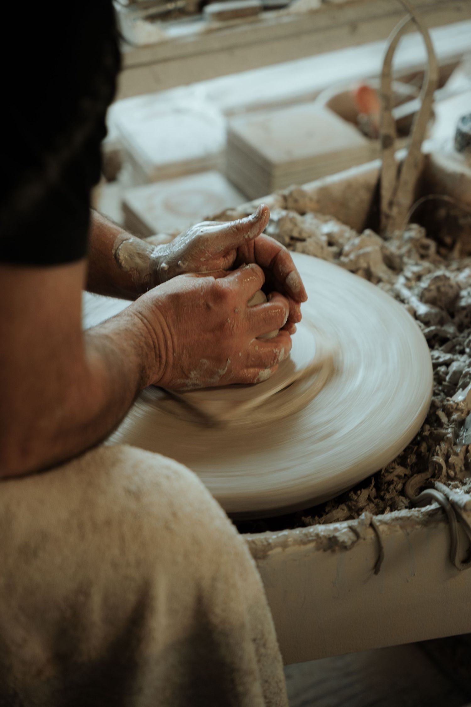 Potter shaping clay on spinning wheel with muddy hands in rustic workshop.