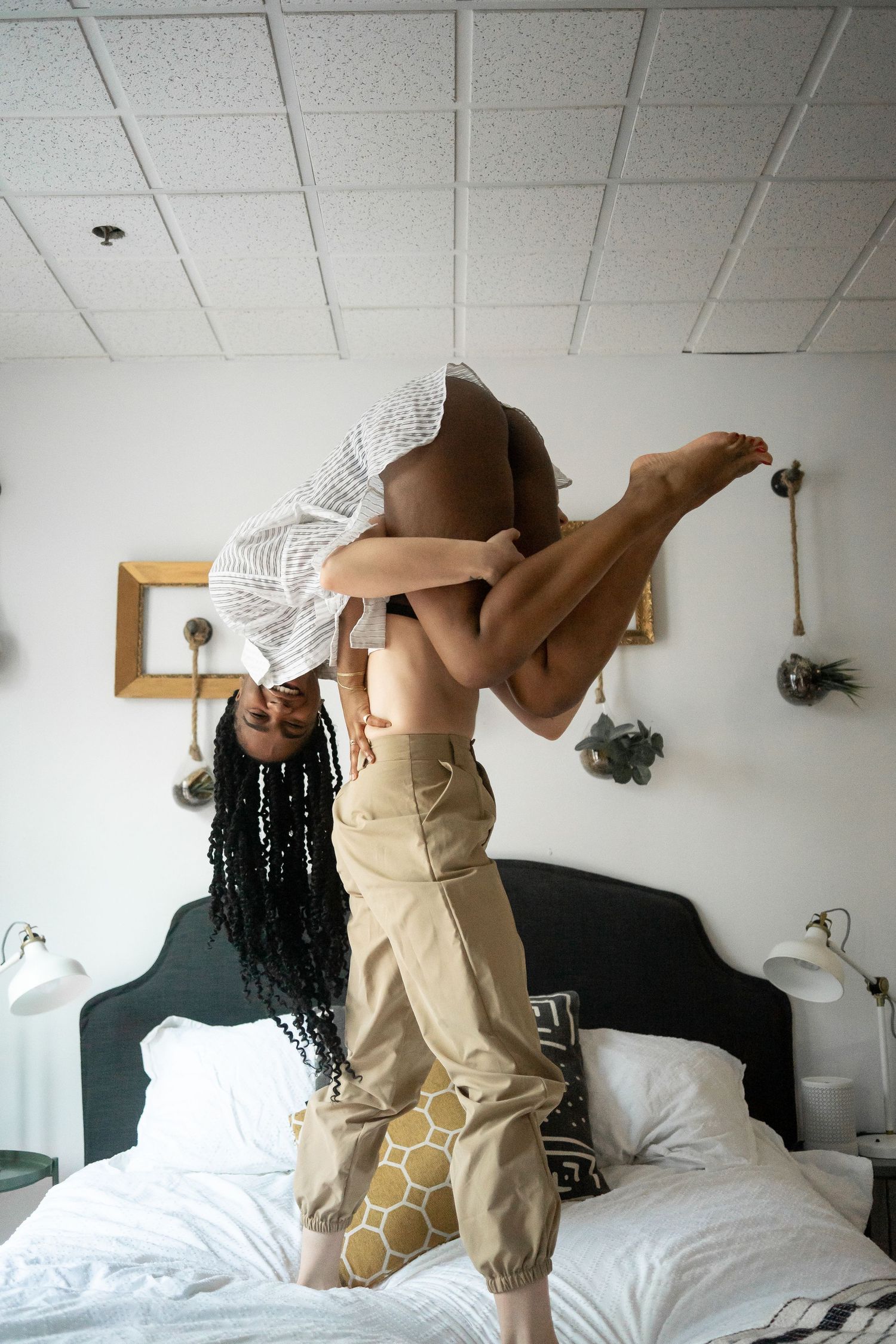 A woman playfully lifting her partner on a bed in a cozy bedroom.