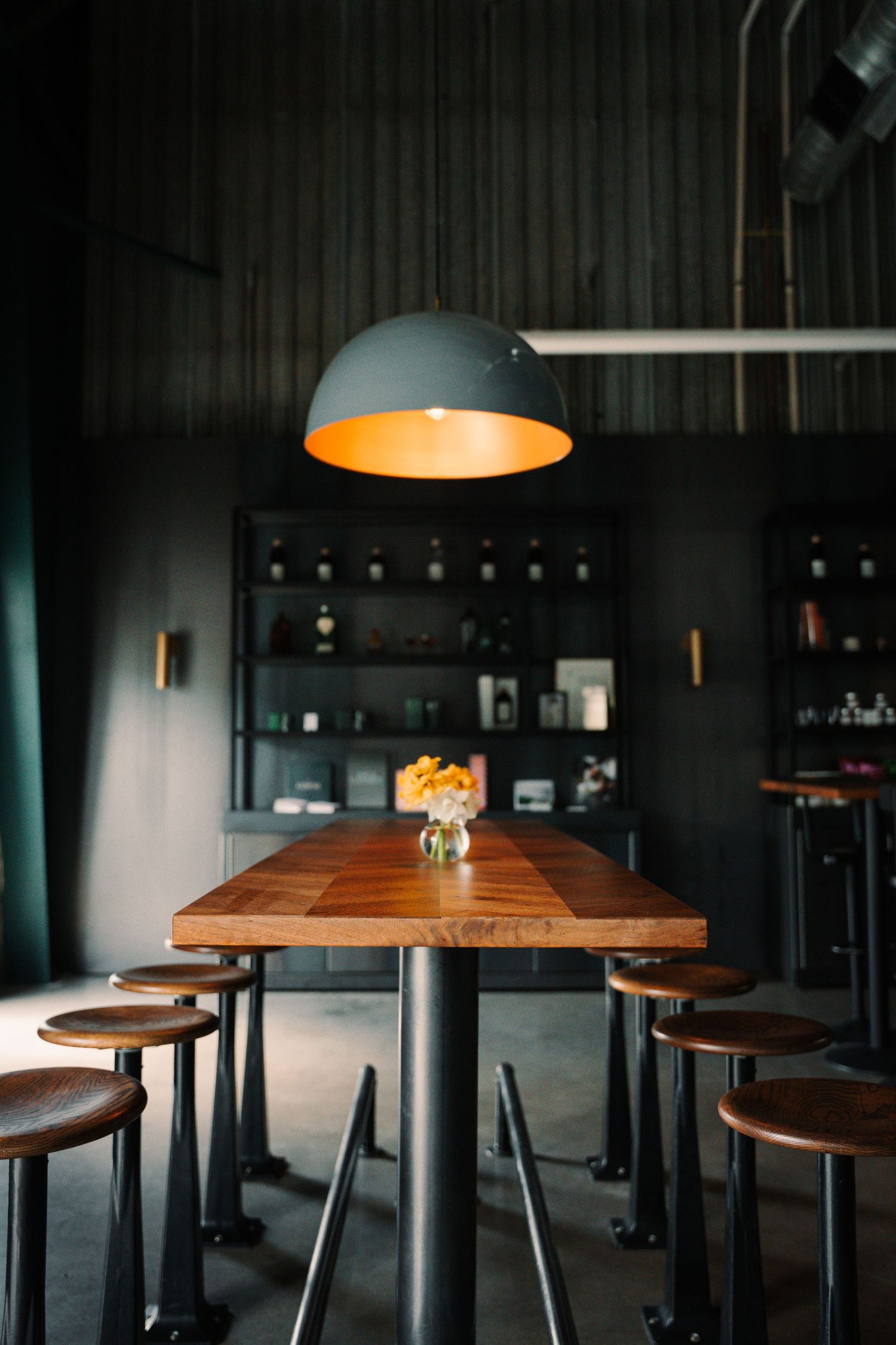 Moody dark dining room with a wooden table, round stools, and a pendant lamp with golden interior.