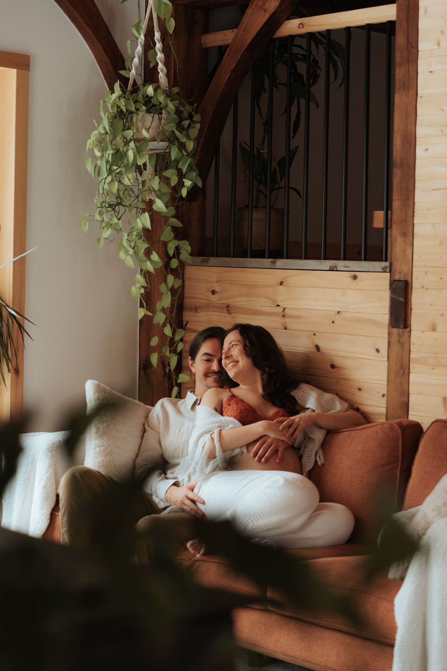 A loving couple cuddles together on a cozy brown sofa in a rustic wooden home with plants.
