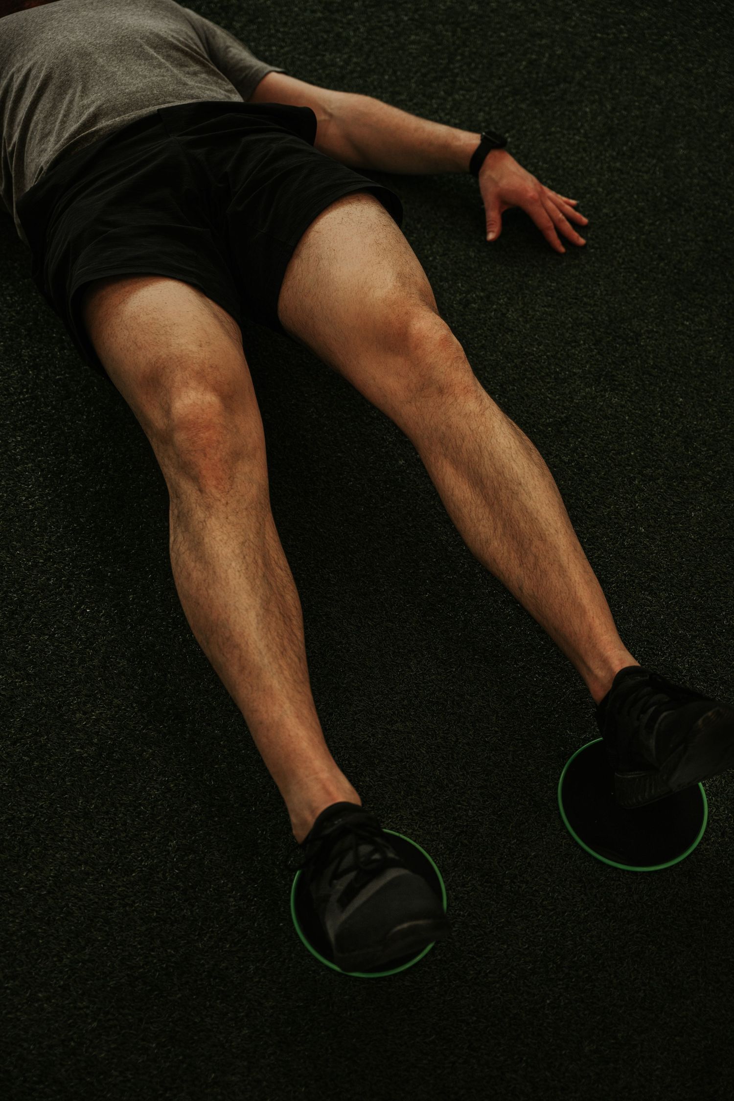 Man lying on gym floor with legs extended, using green disc sliders for core exercise.