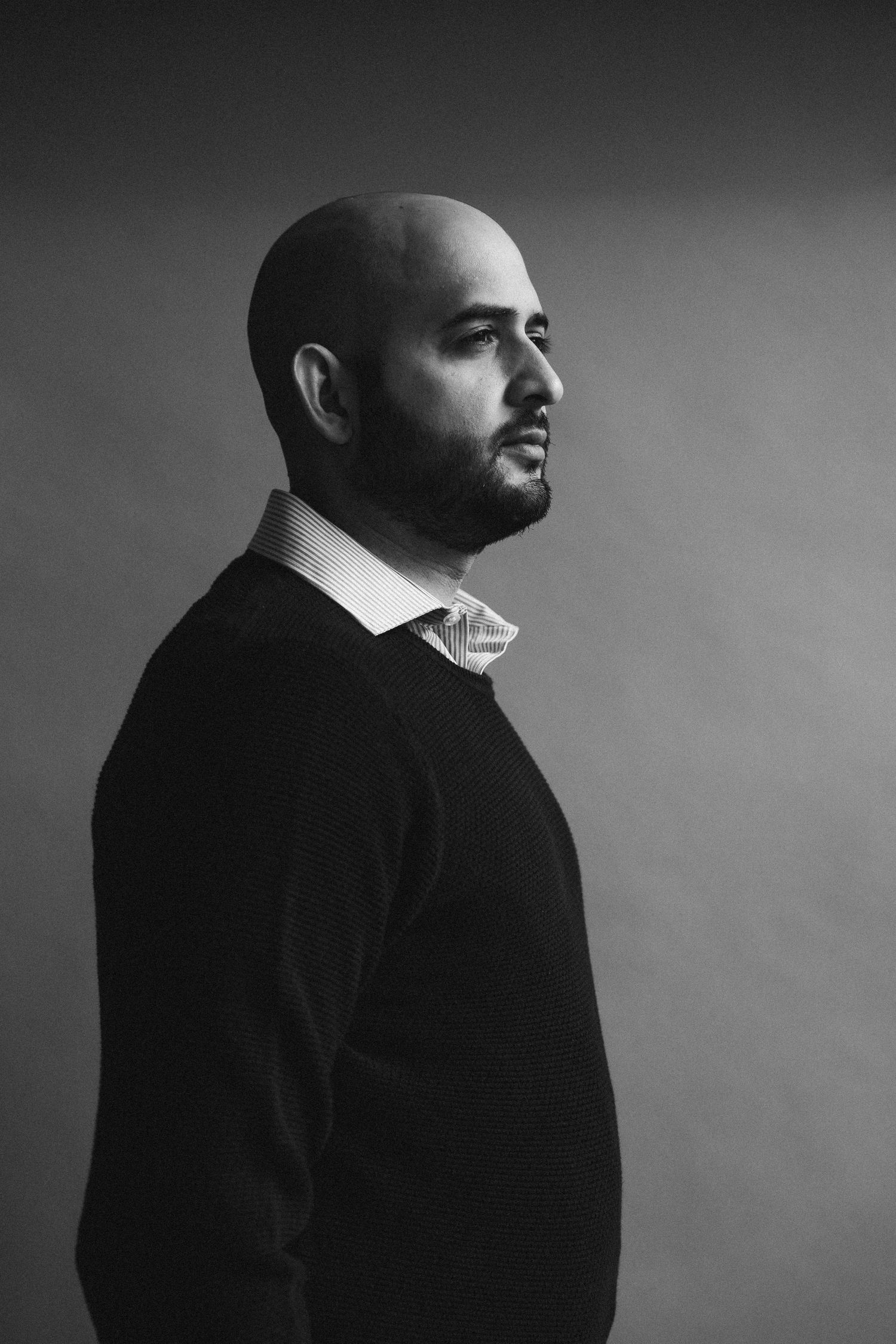 Black and white profile portrait of bald bearded man in sweater.