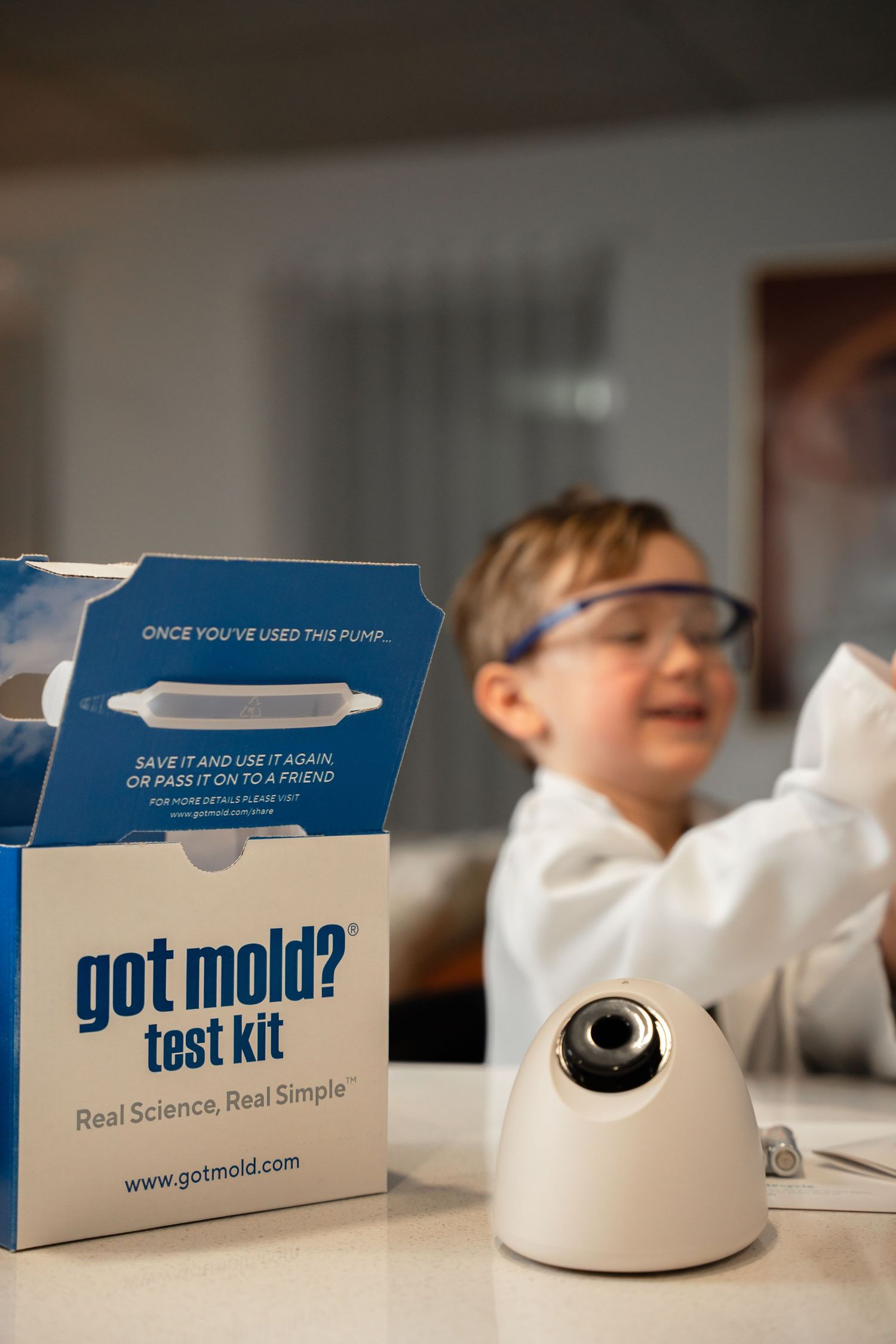 Got Mold test kit box on counter with smiling child in lab coat and safety goggles.