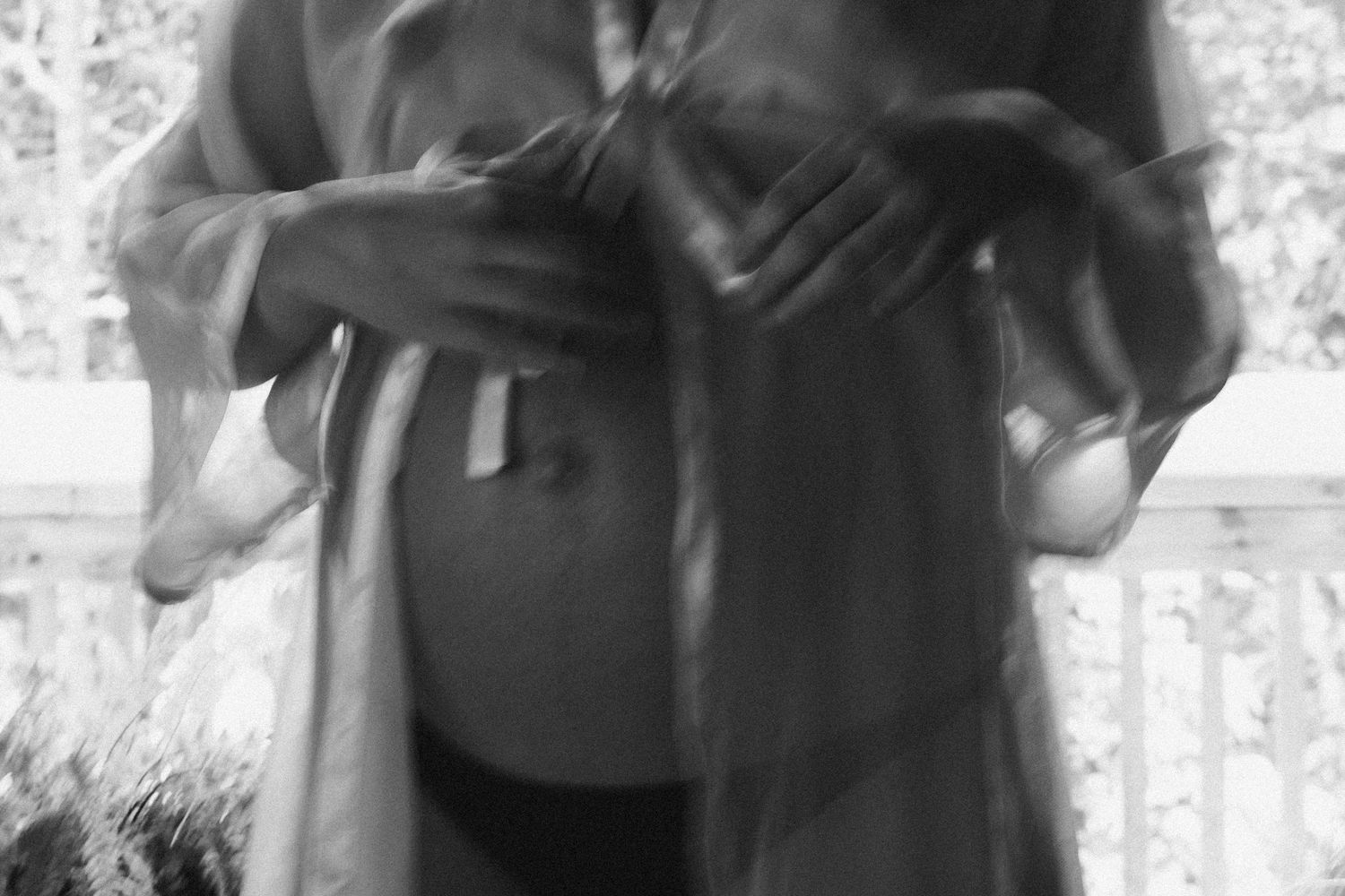 Black and white blurred portrait of a pregnant woman cradling her baby bump outdoors.