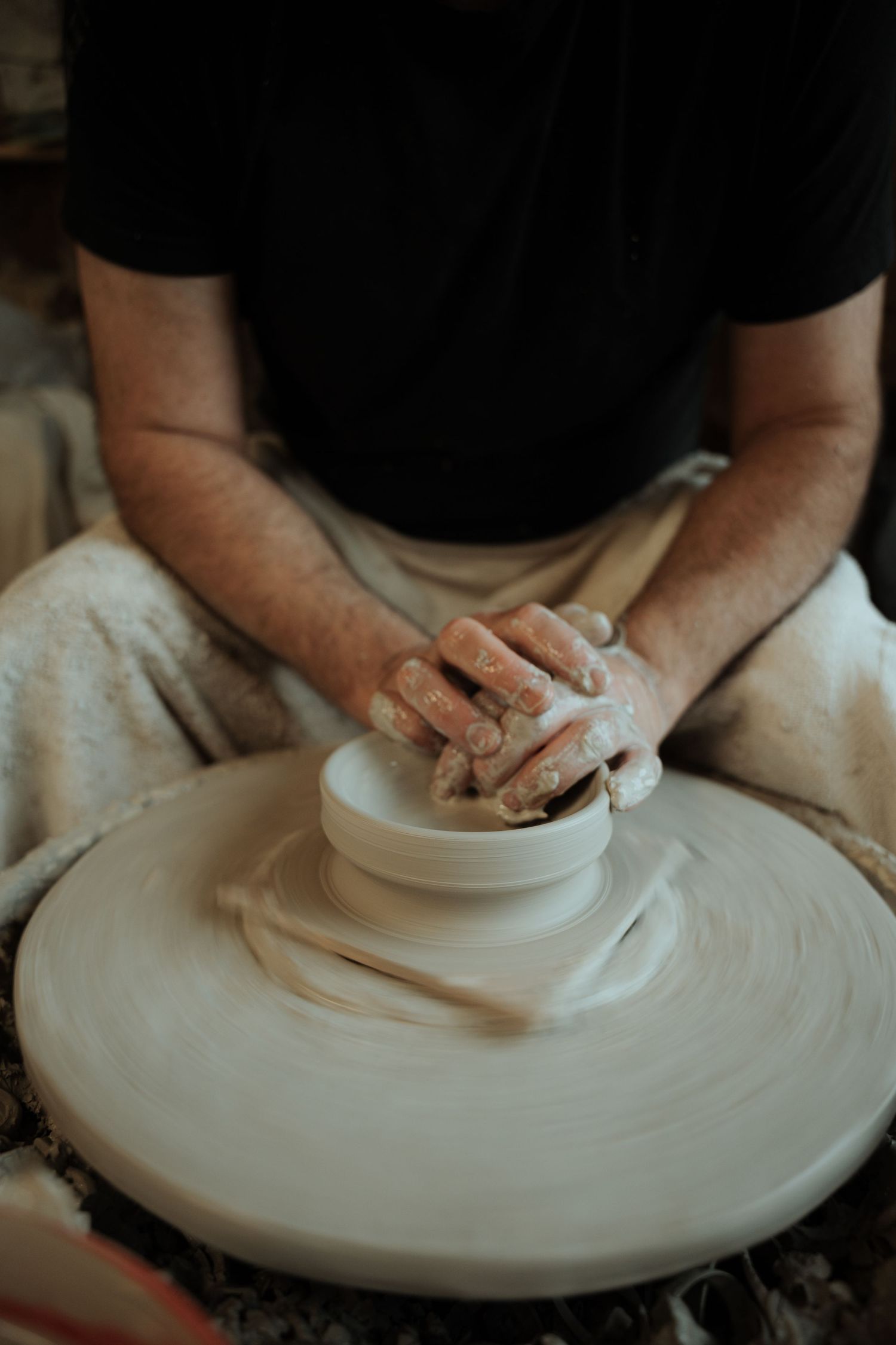 Potter shaping white clay on a spinning wheel with clay-covered hands in a pottery studio.