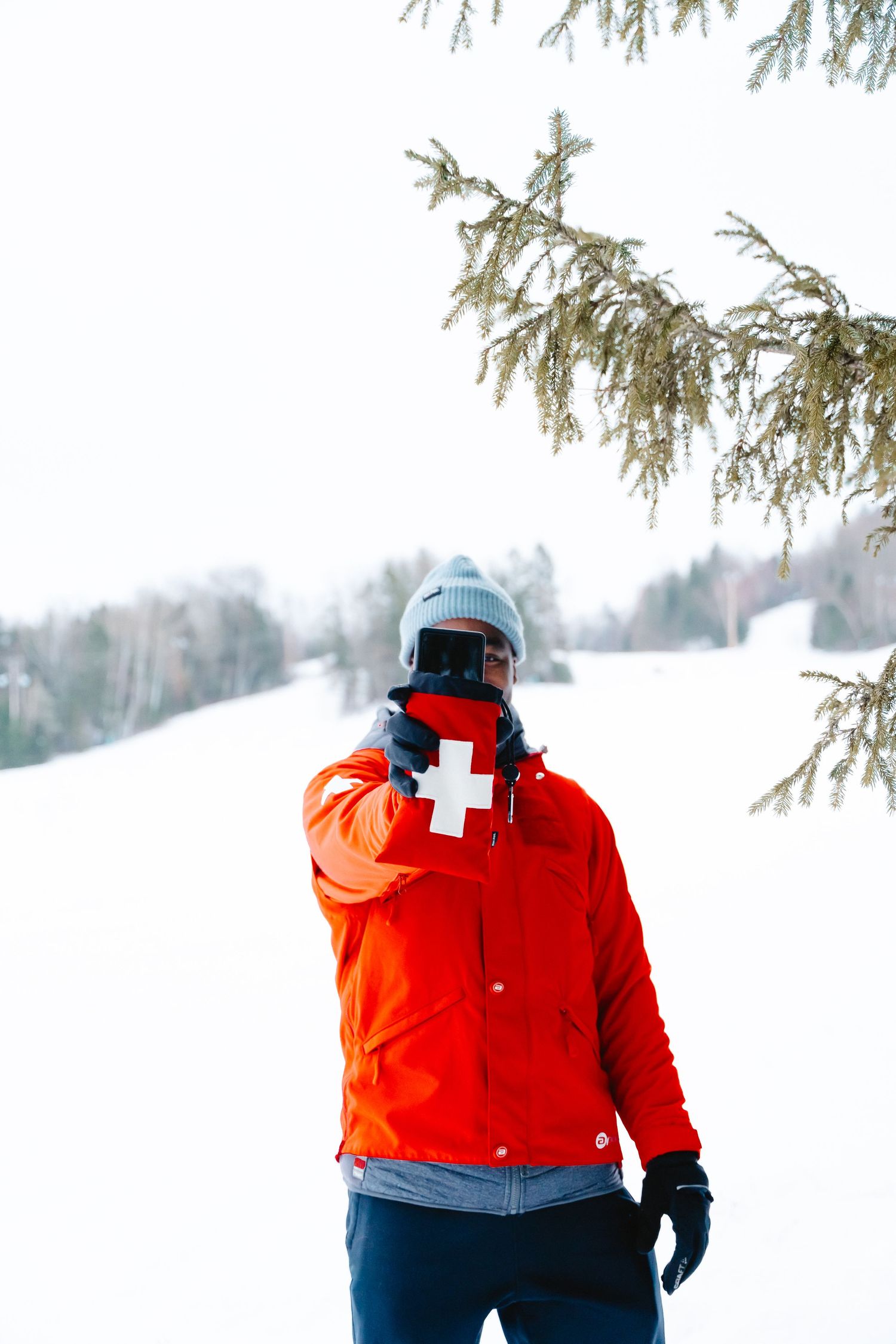 Ski patrol member in red jacket with white cross pointing finger in a snowy winter landscape.