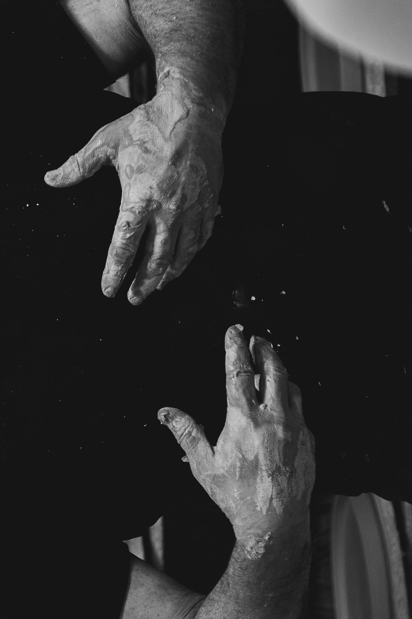 Black and white photo of two chalked hands reaching toward each other against a dark background.