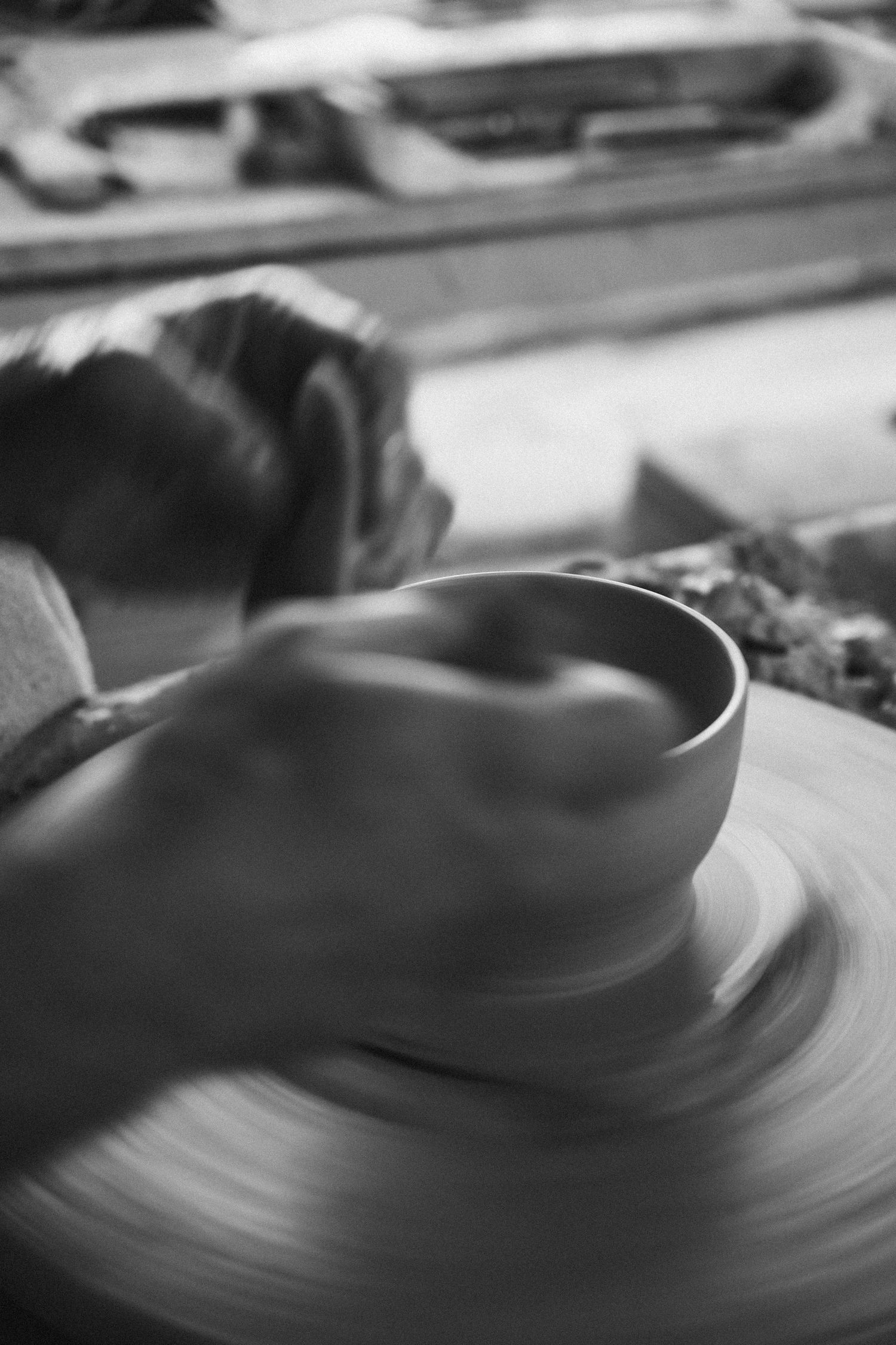 Black and white blurred motion shot of potter shaping clay bowl on spinning pottery wheel.