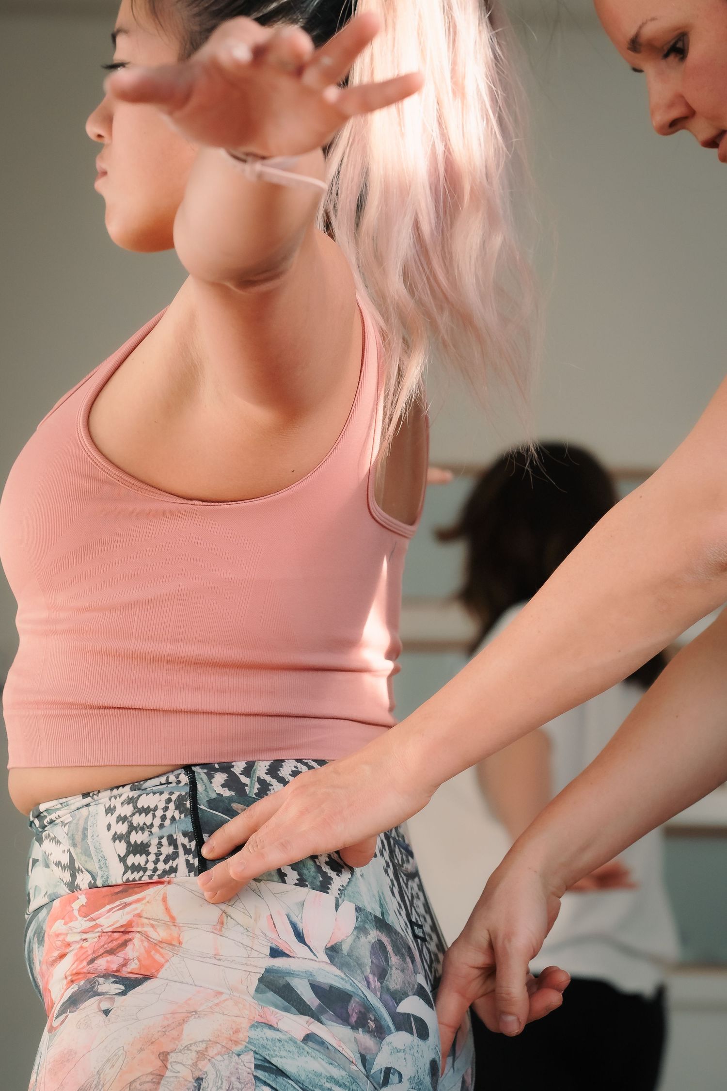Yoga instructor adjusting student's hip alignment during a standing pose in a yoga class.