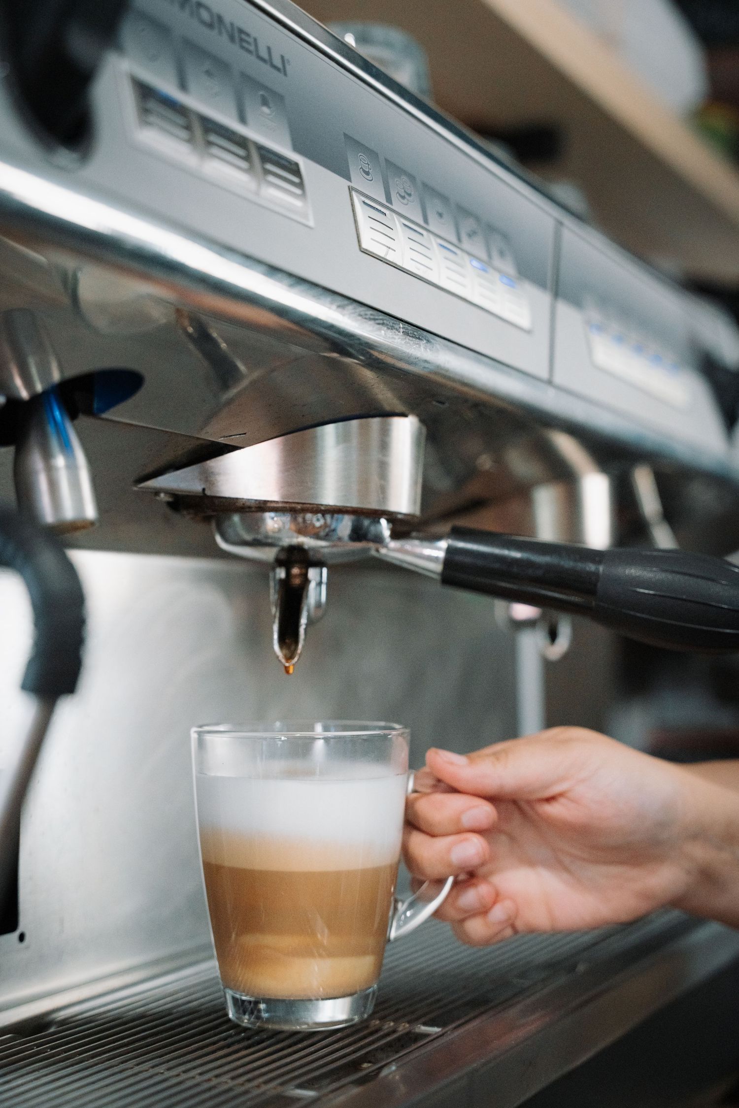 Espresso machine dispensing coffee into a glass latte cup held by a barista.