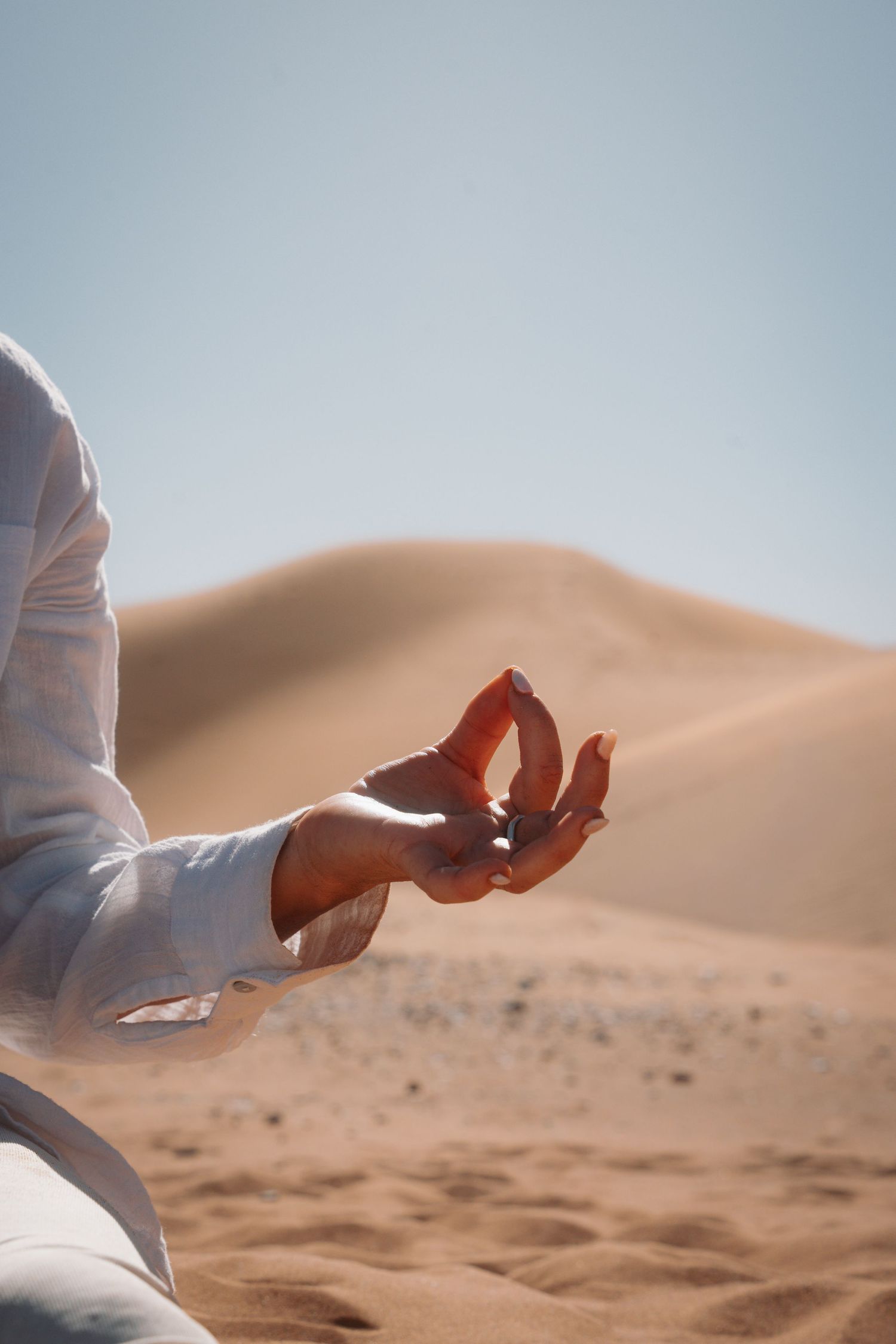 Close-up of person in white linen holding a gentle mudra hand gesture in the desert.
