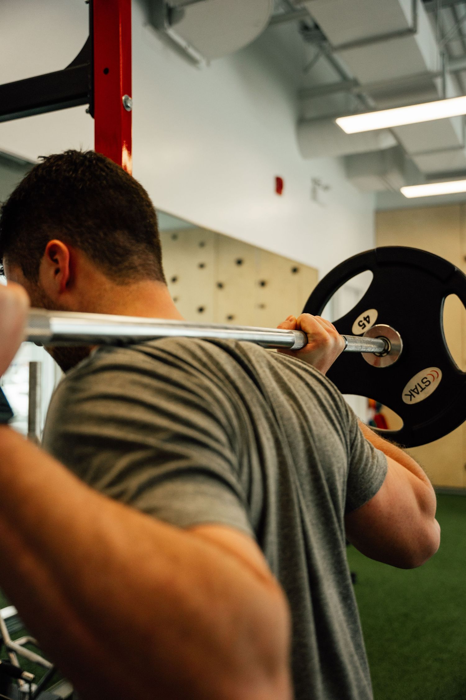 Male athlete performing barbell back squat exercise in modern gym with red squat rack.