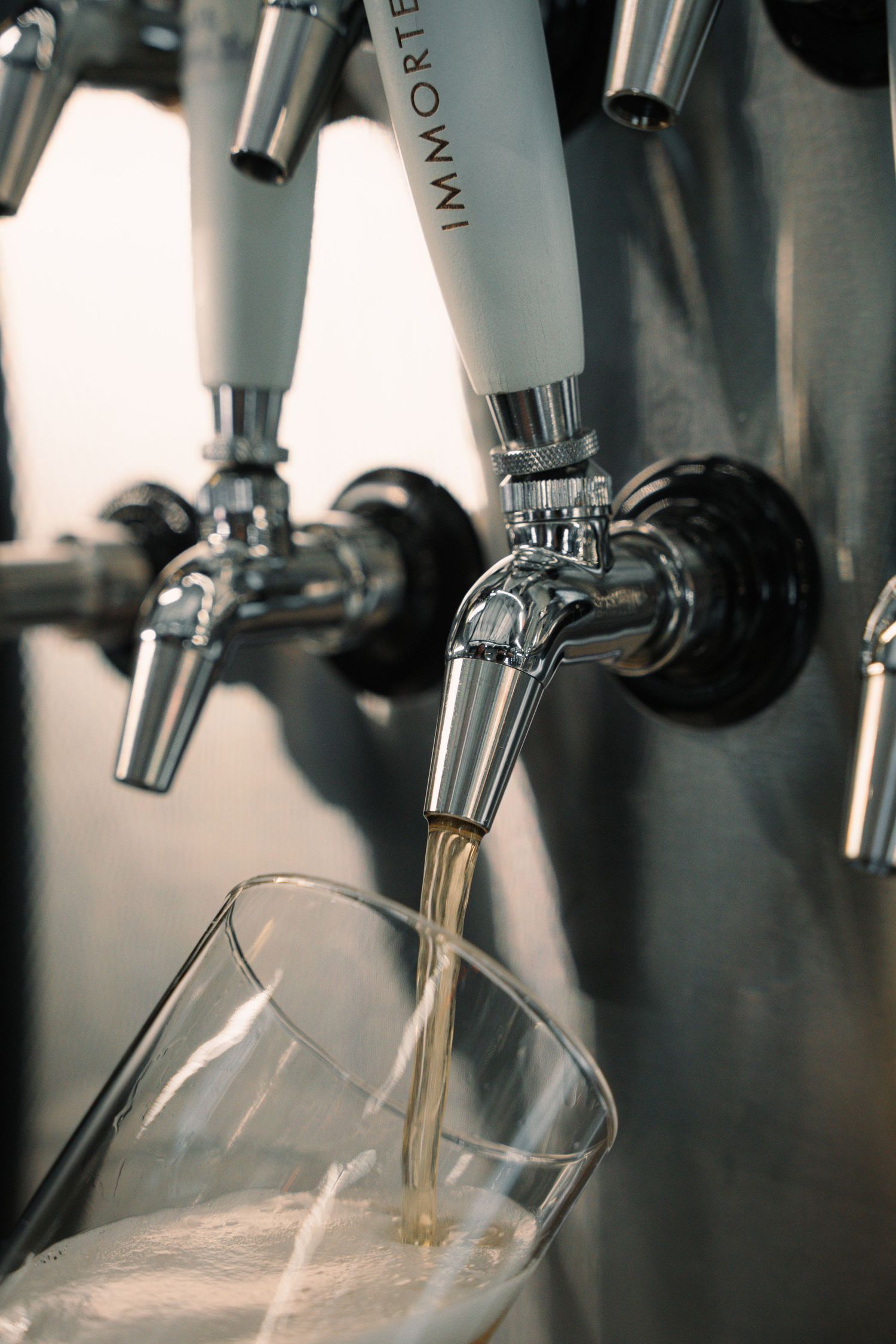 Beer being poured from an Immortal tap handle into a glass at a craft brewery bar.