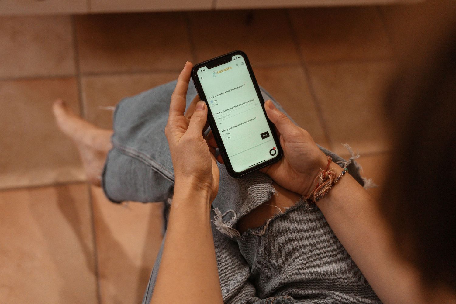 Person sitting on tiled floor using a smartphone displaying a minimalist app interface on screen.