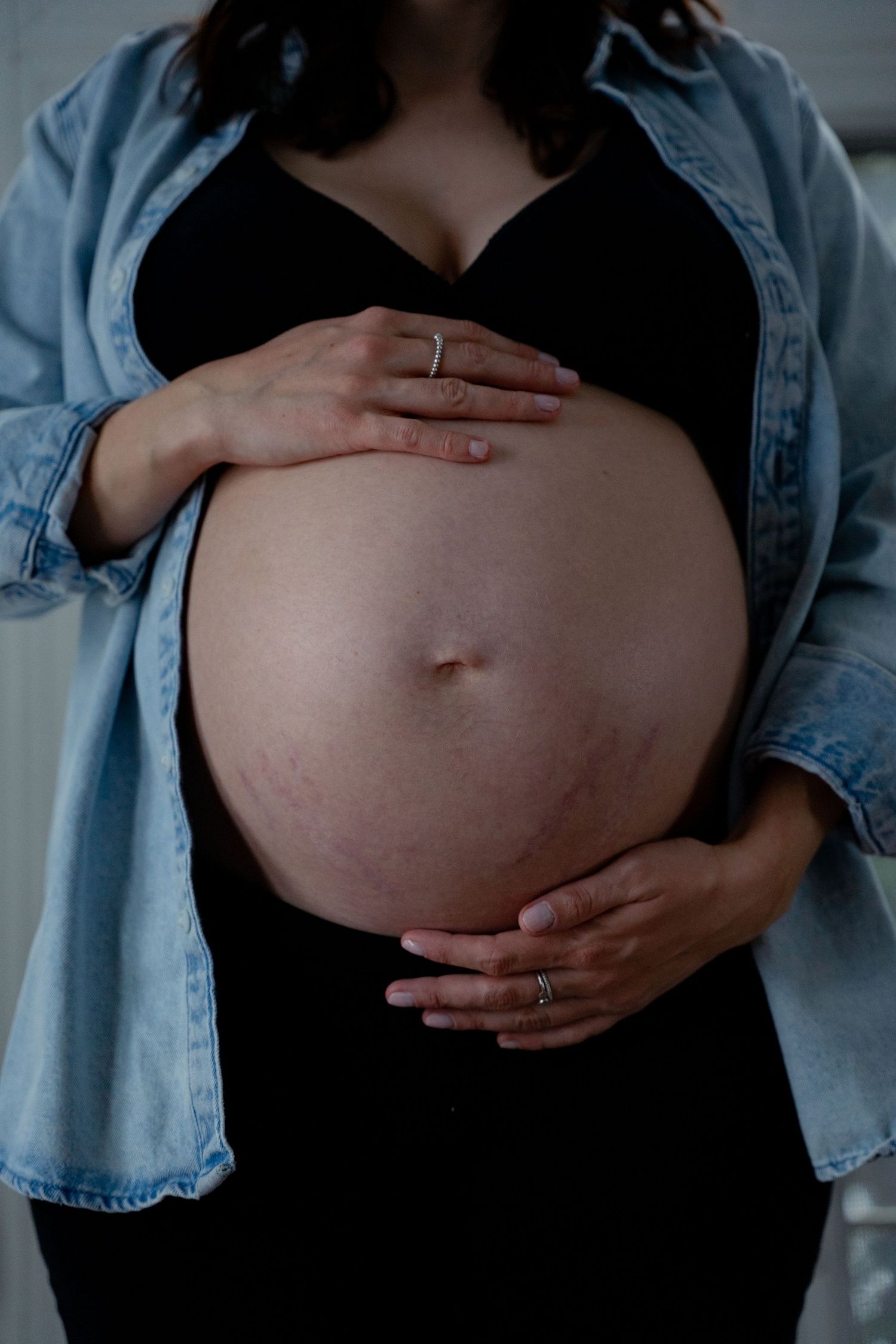 Pregnant woman in denim jacket and black outfit cradling her bare baby bump.