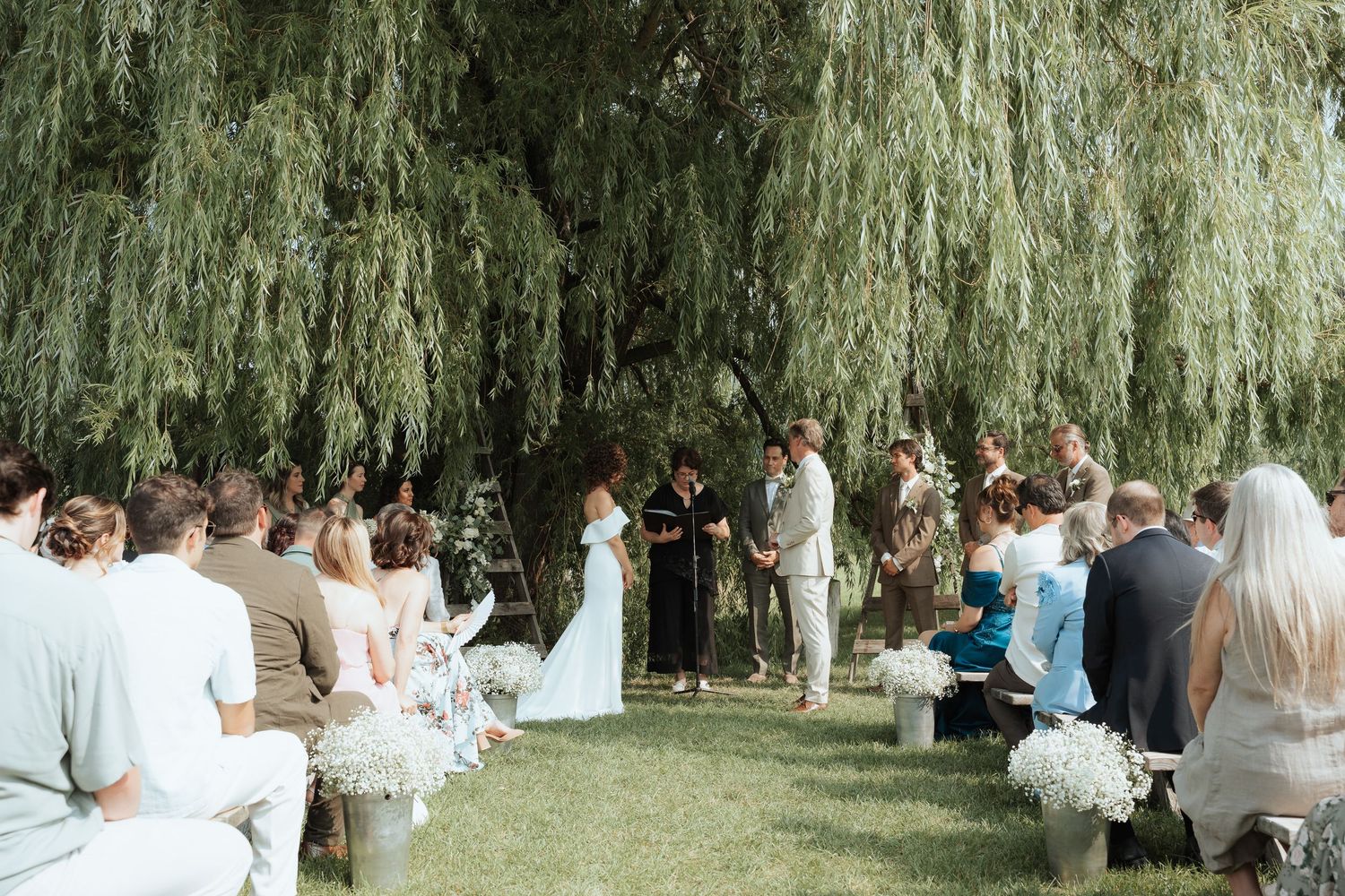 Outdoor wedding ceremony under a weeping willow tree with guests seated on both sides.