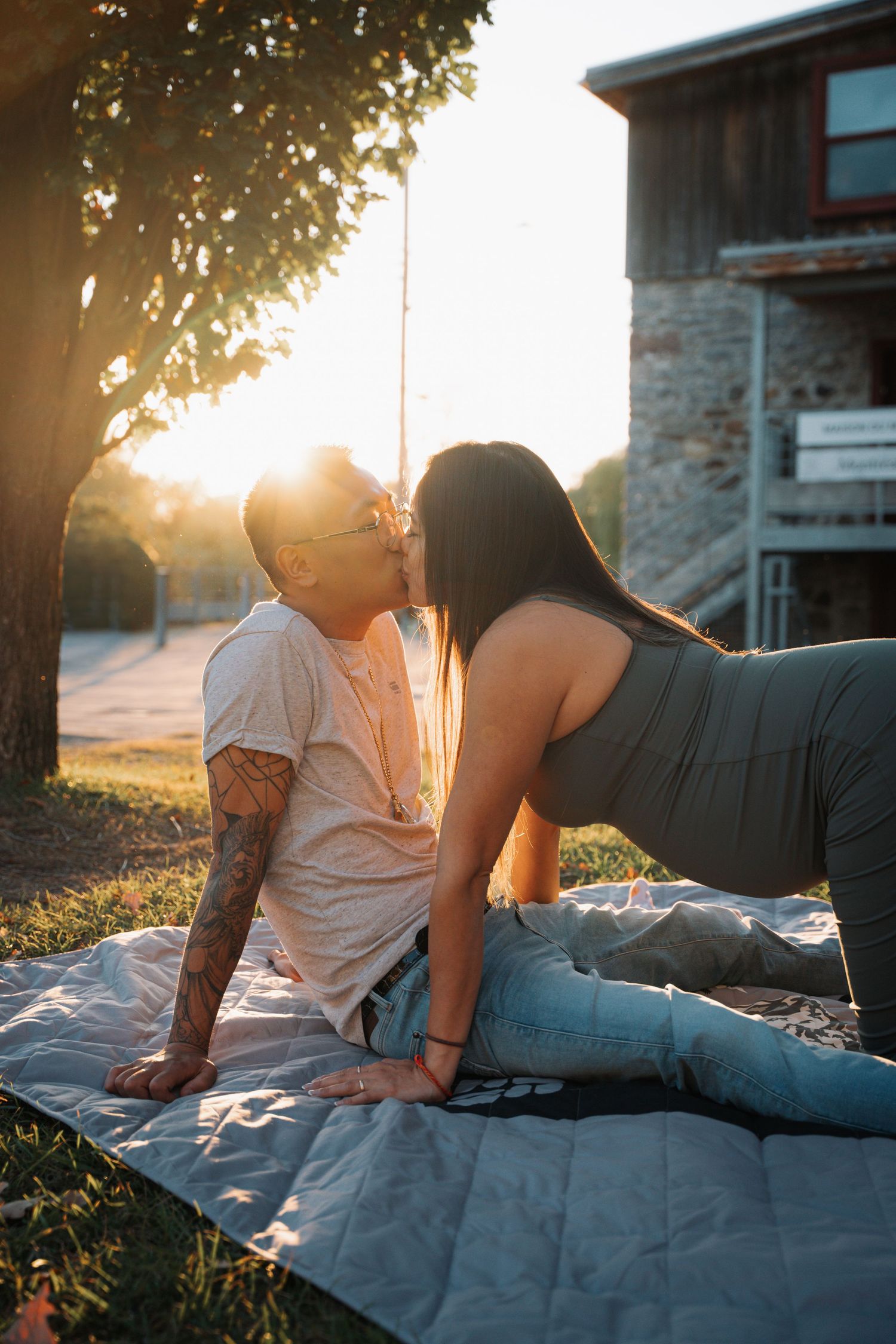 Couple sharing a tender kiss while sitting on a blanket in a sunlit park during golden hour.