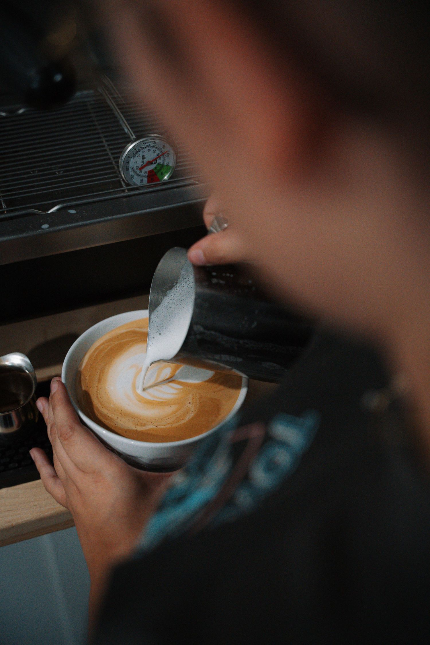 Barista pouring steamed milk to create latte art in a white ceramic cup.