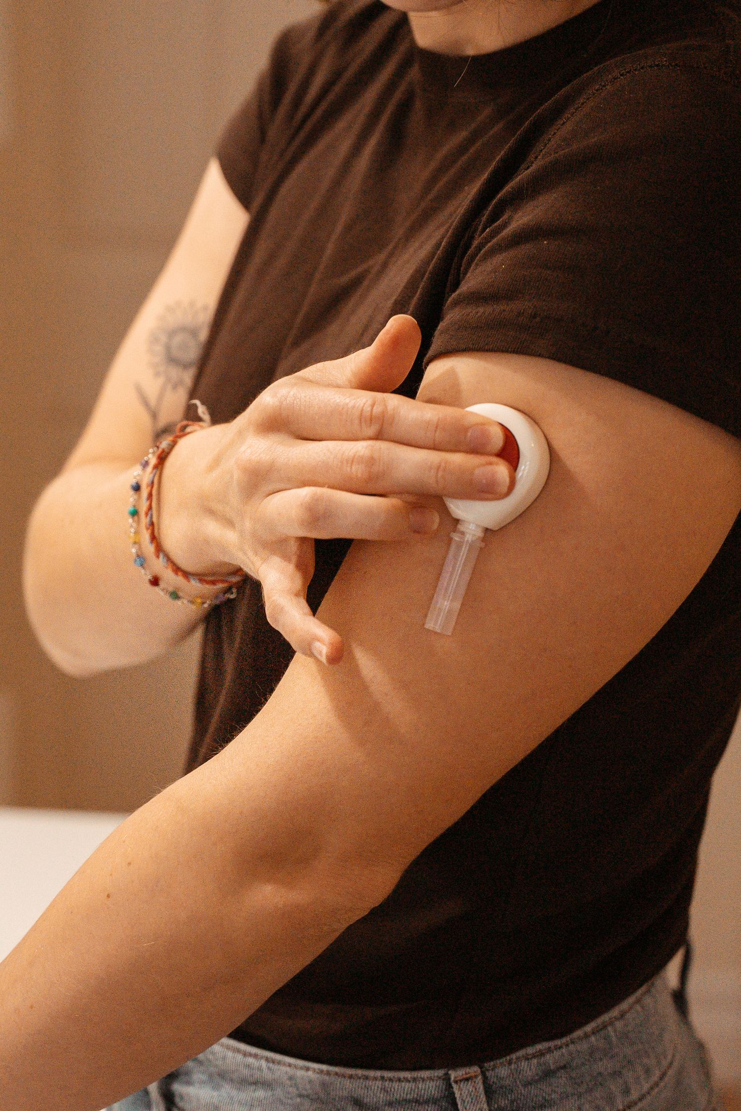 Person applying a continuous glucose monitor sensor to their upper arm.