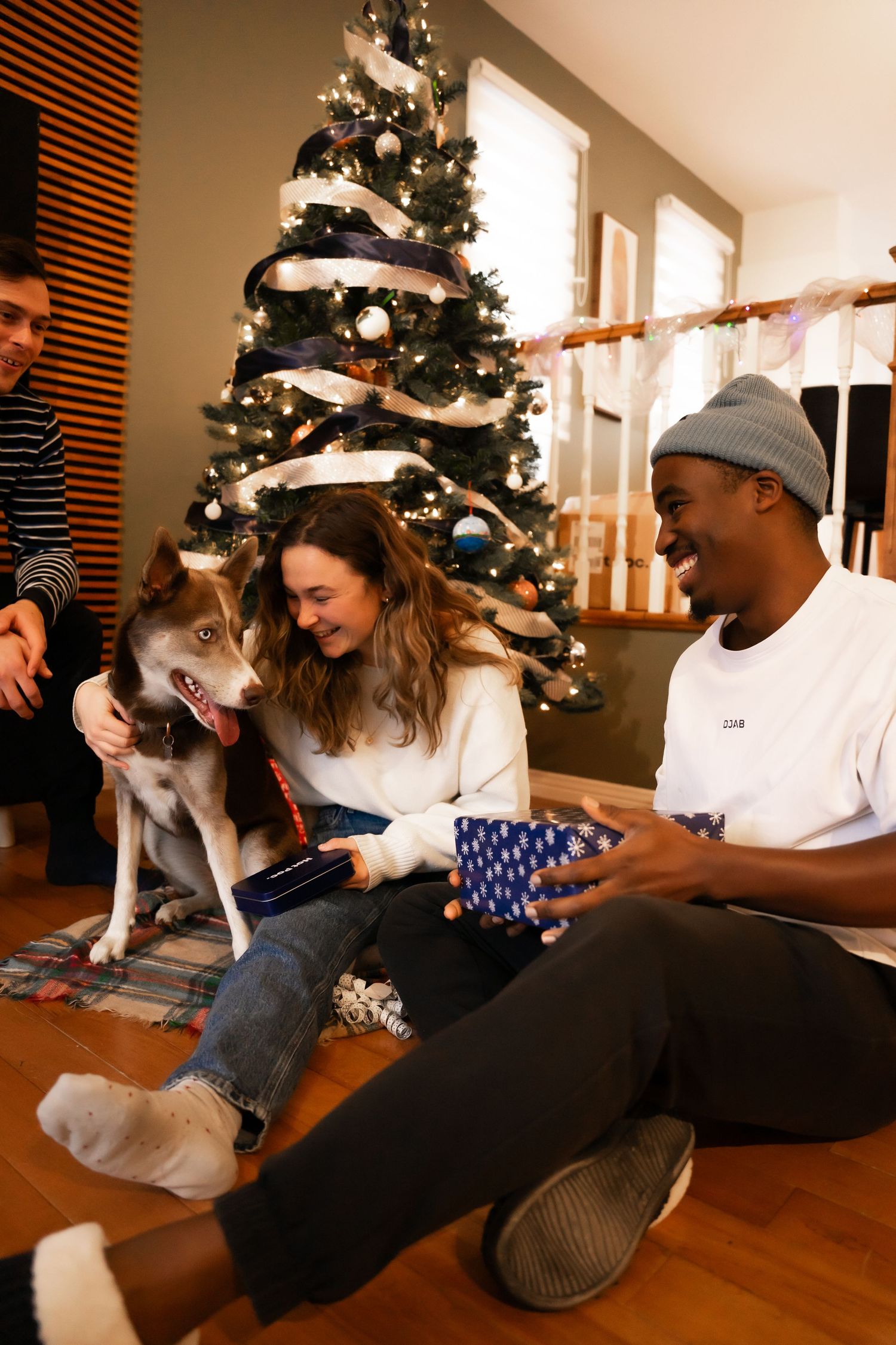 Friends and dog celebrating Christmas together near decorated tree opening gifts indoors.