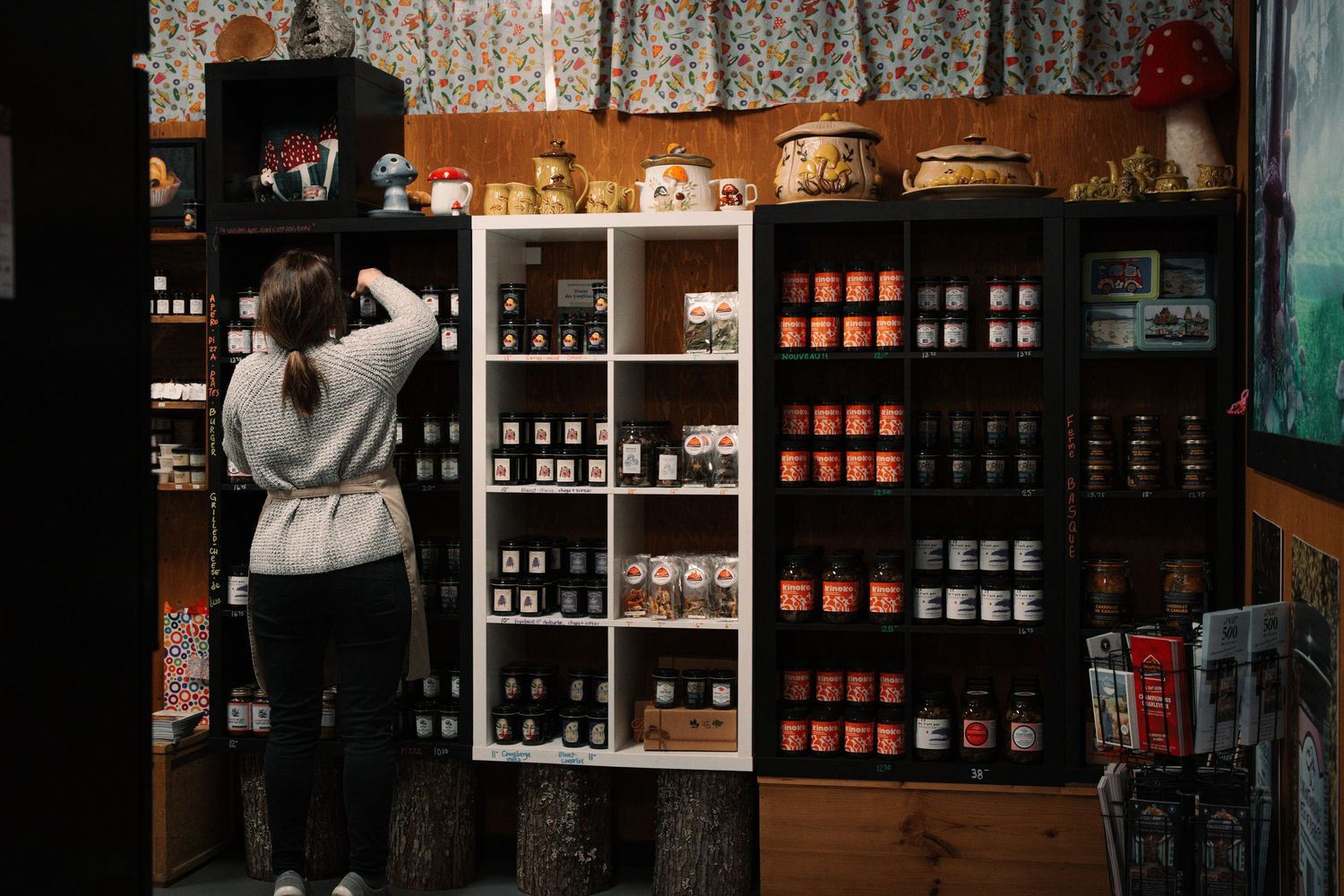 Woman browsing shelves of artisan jars and bottles in a rustic specialty food shop.