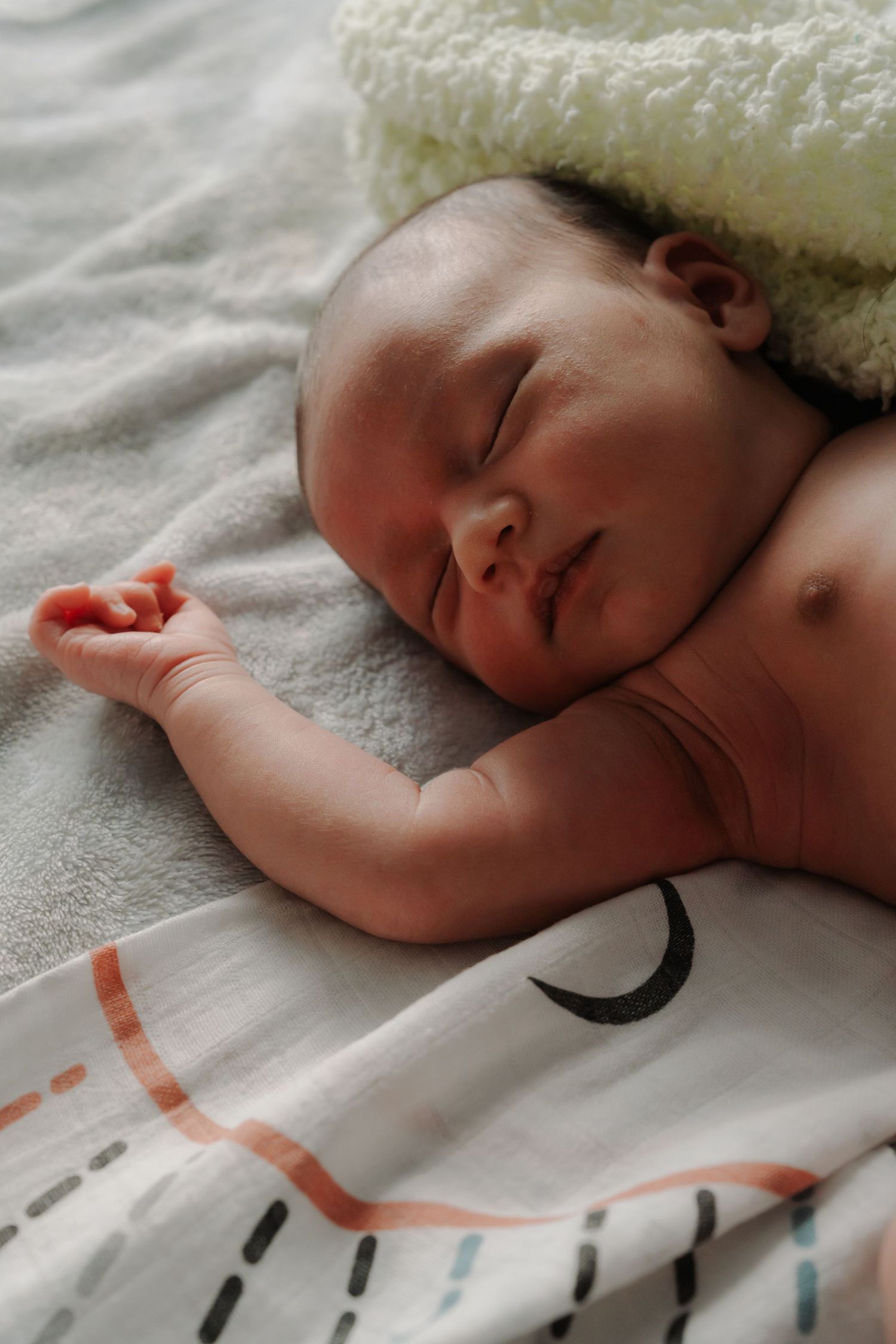 Peaceful newborn baby sleeping on soft blanket with tiny hand raised.