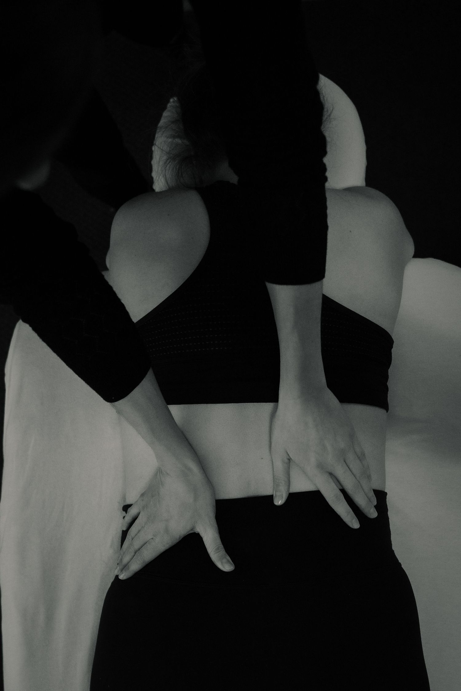 Black and white artistic photo of massage therapist performing lower back treatment on client.