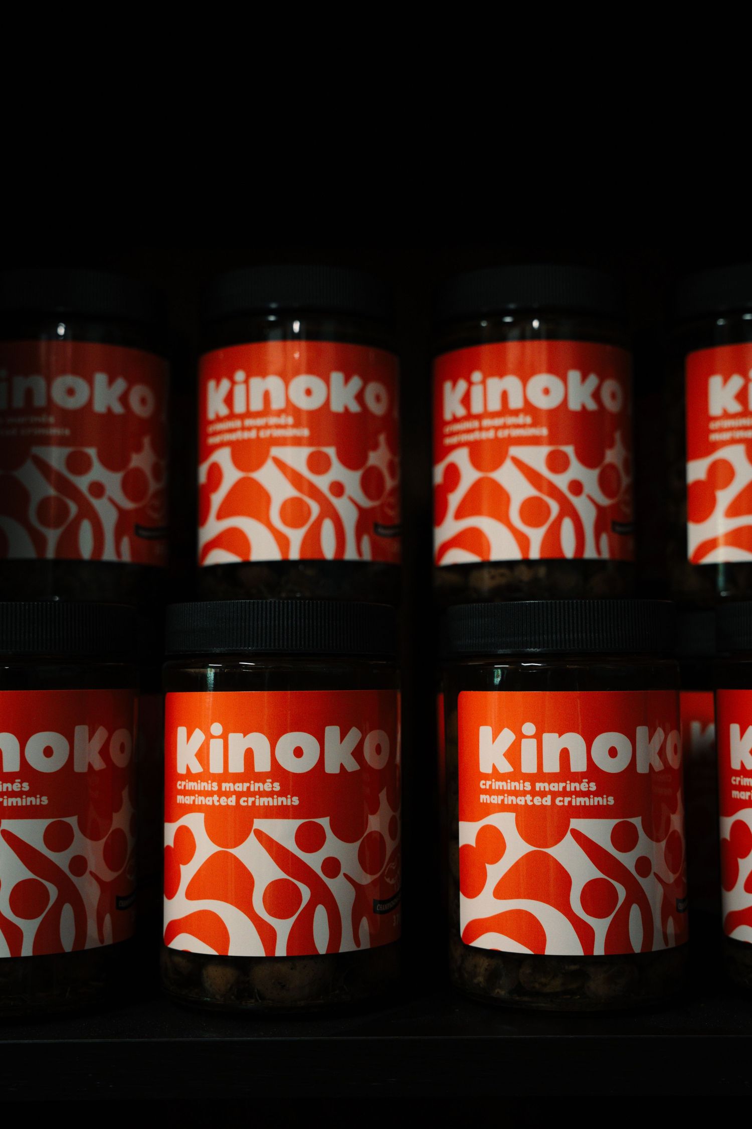 Shelves stocked with red and white Kinoko marinated crimini mushroom jars in a dark display setting.
