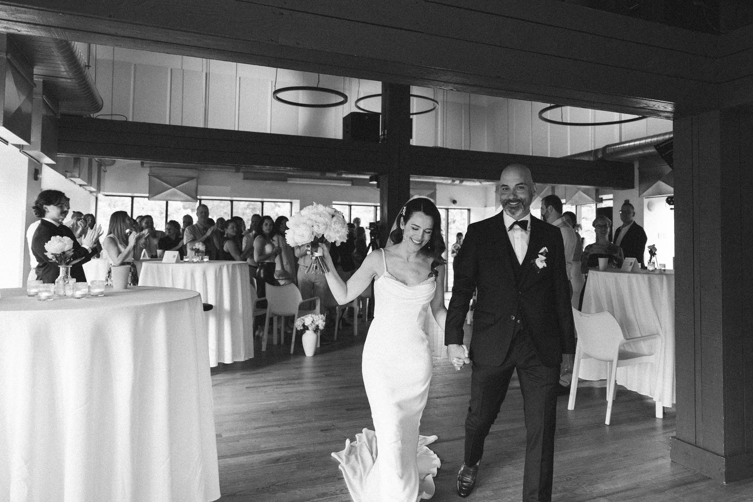 Black and white photo of bride and groom making grand entrance at elegant wedding reception venue.