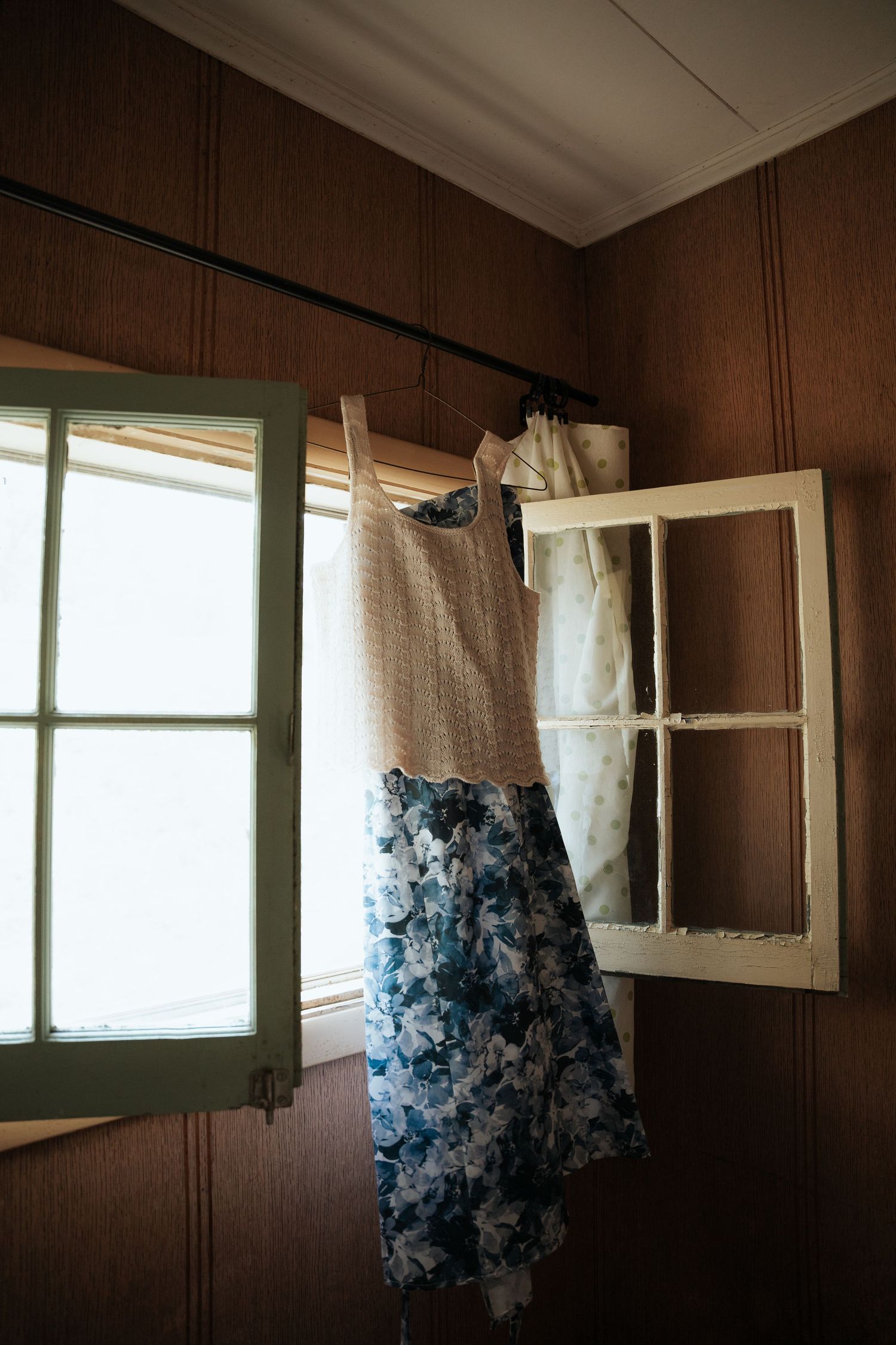 Floral blue and beige wedding dress hanging near a vintage window frame in a rustic room.