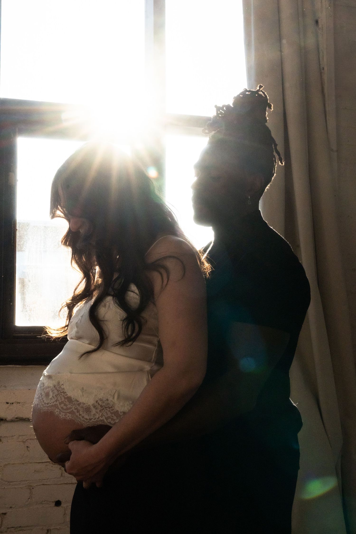 Silhouette of pregnant woman and partner backlit by bright sunlight through window.
