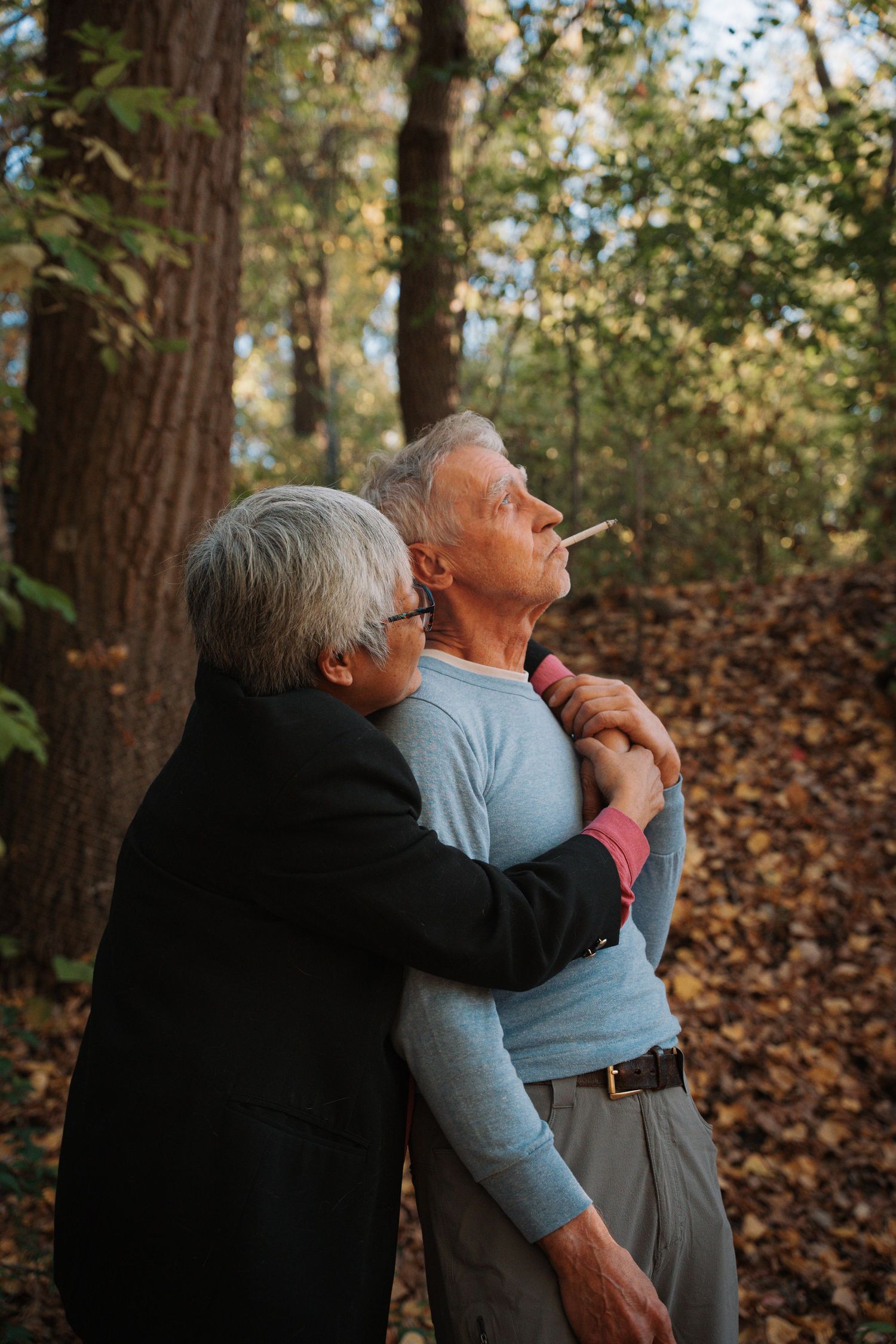 Elderly woman hugging man from behind while looking up in forest.