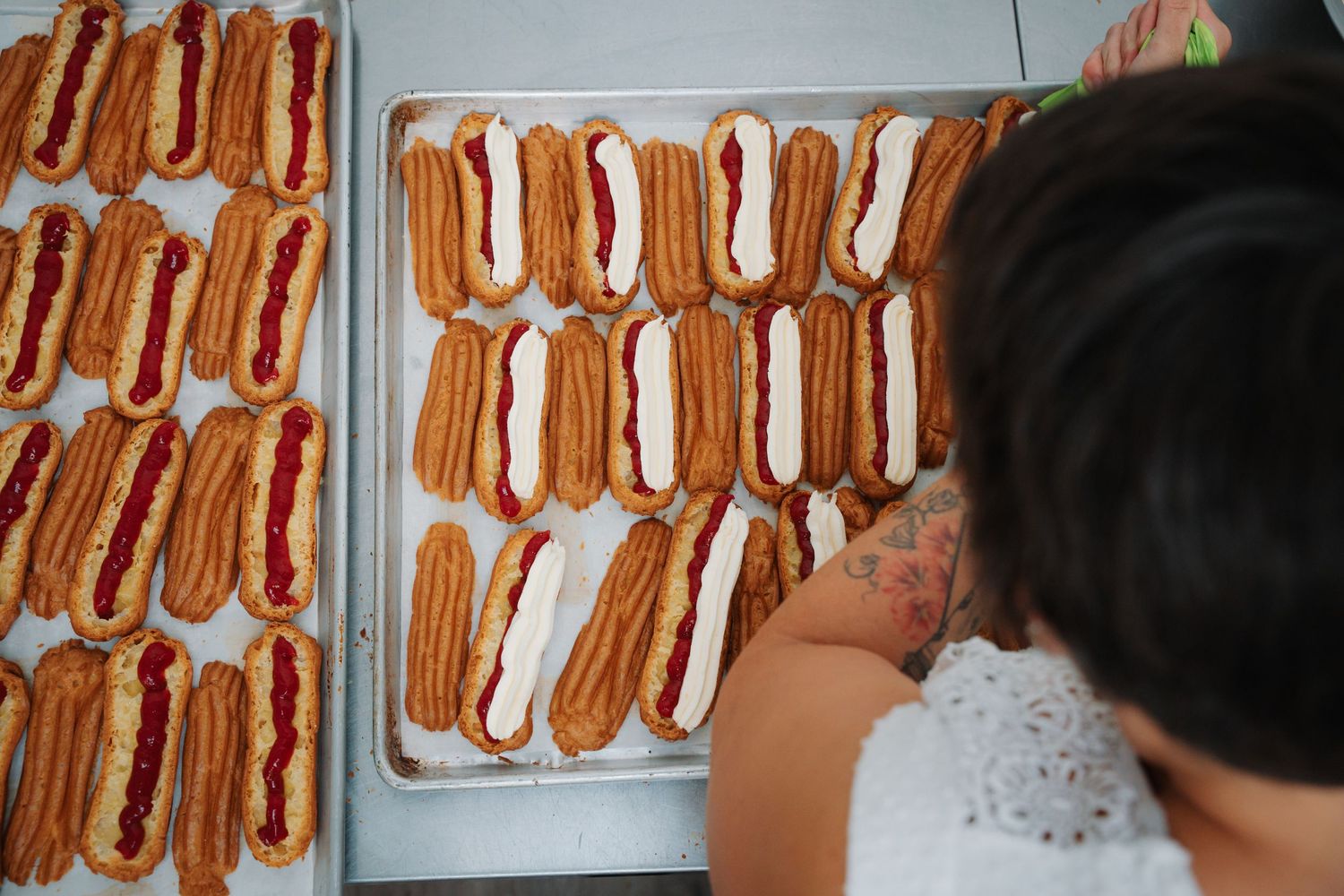 Overhead view of trays of filled churros with cream and jam toppings at bakery.