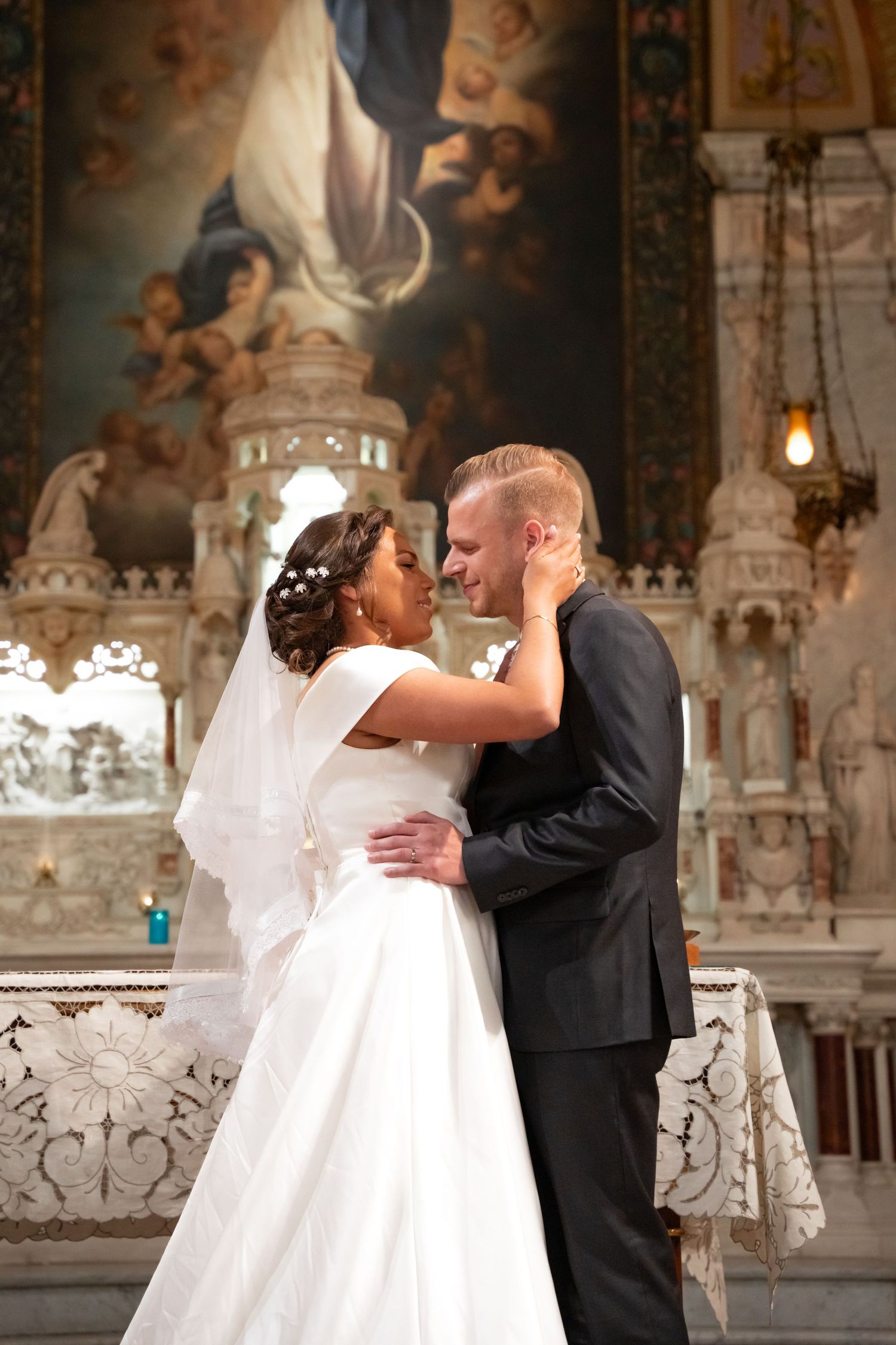 Newlywed couple sharing romantic moment at ornate church altar, bride in white gown and veil.