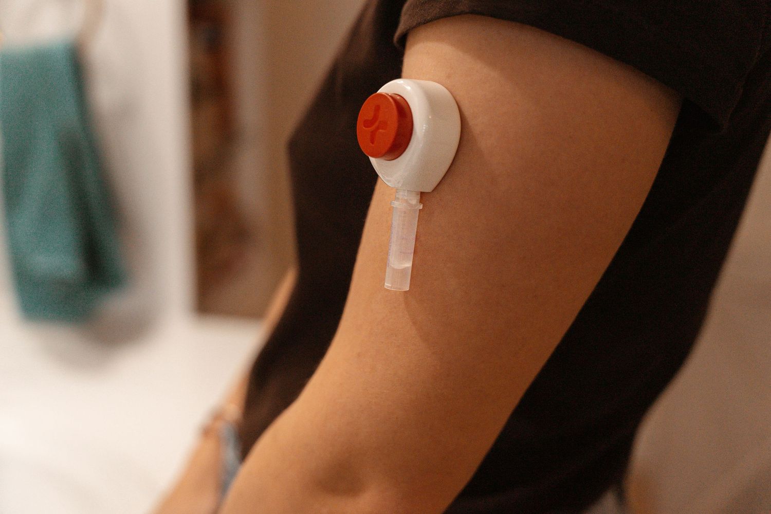 Close-up of a white and red medical patch device applied to a person's upper arm.