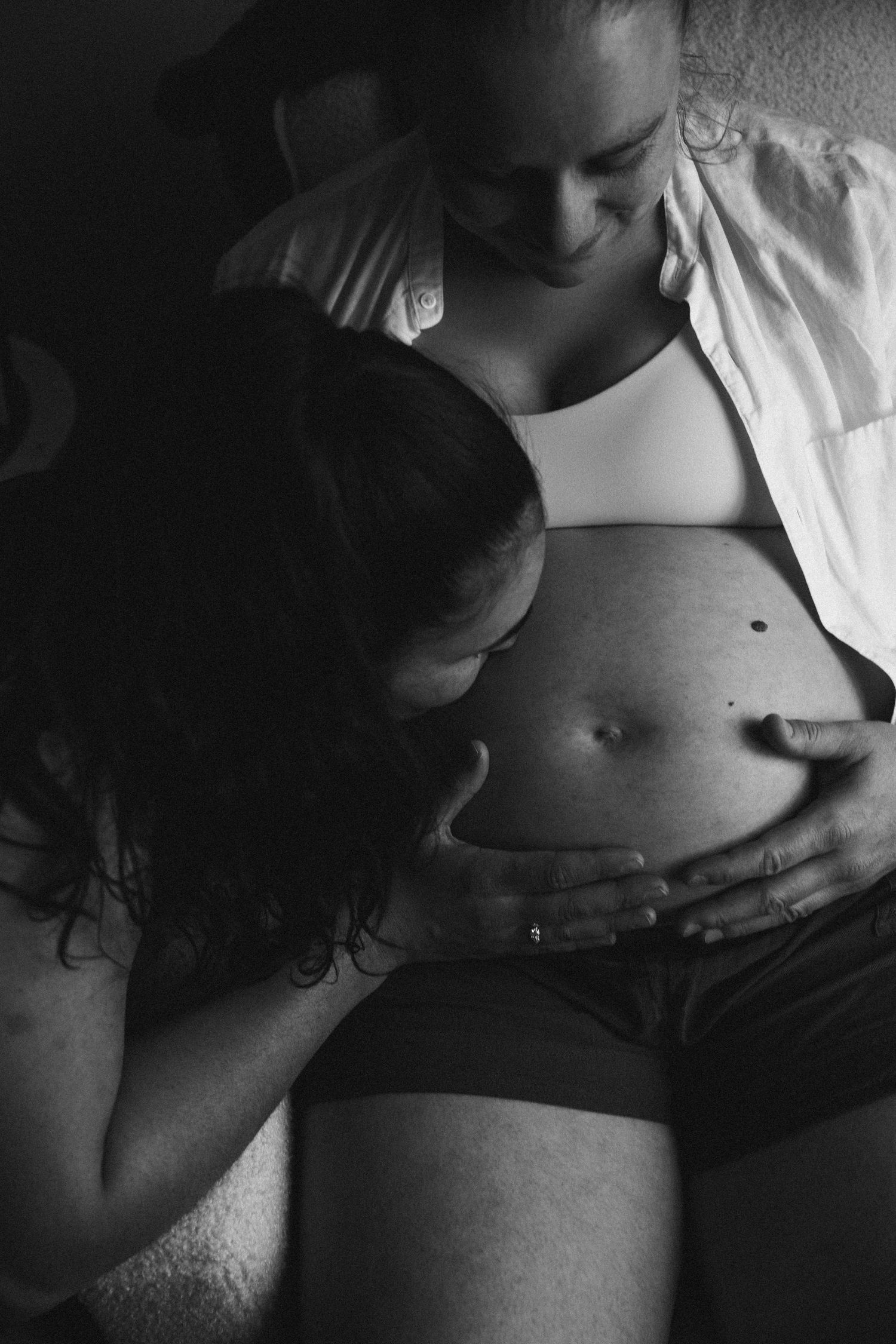 A black and white intimate photo of a person resting their head on a pregnant womans baby bump.
