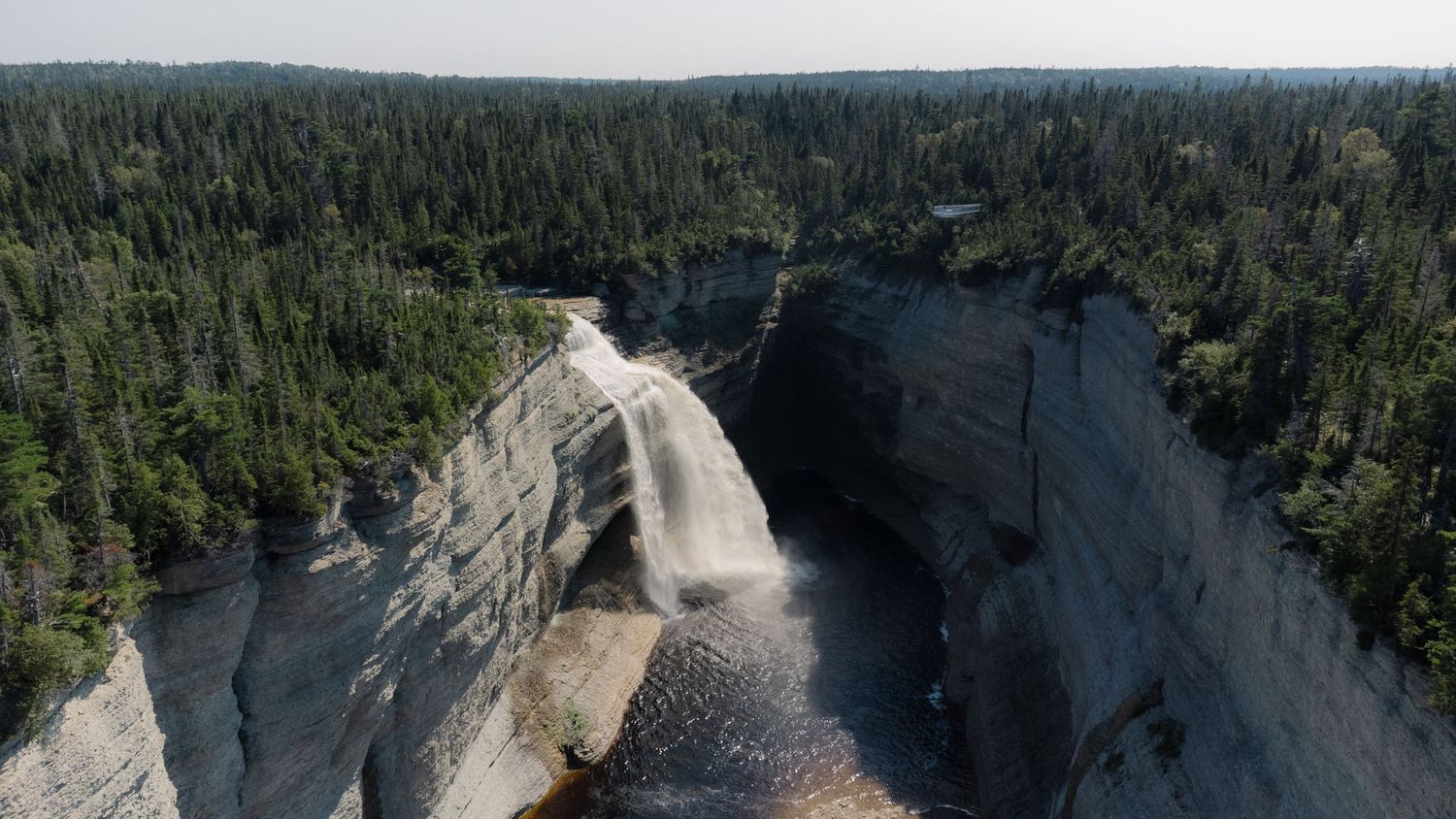 Aerial view of a stunning waterfall cascading over grey limestone cliffs surrounded by dense forest.